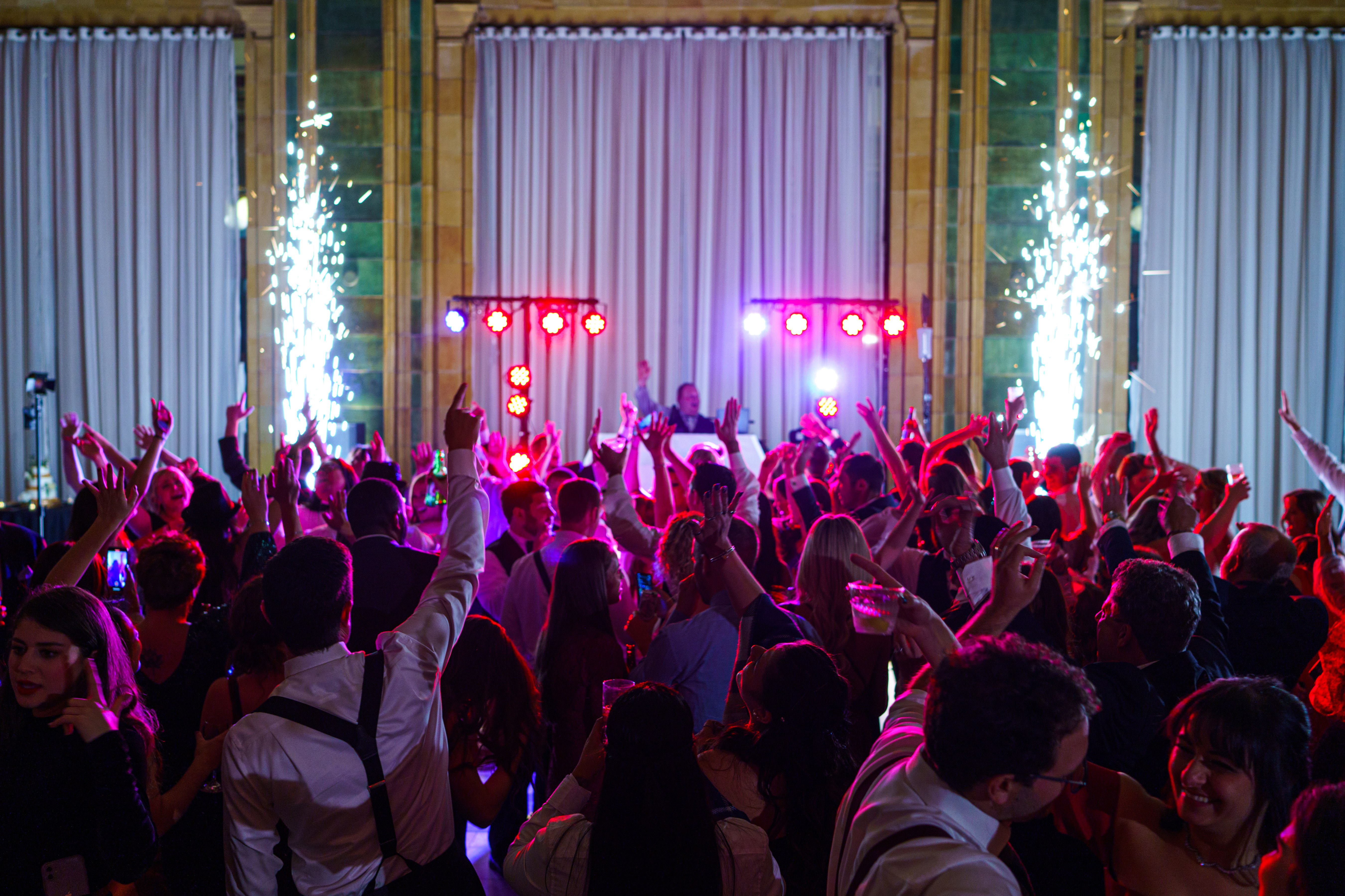 Guests celebrating beneath event lighting and spark fountains