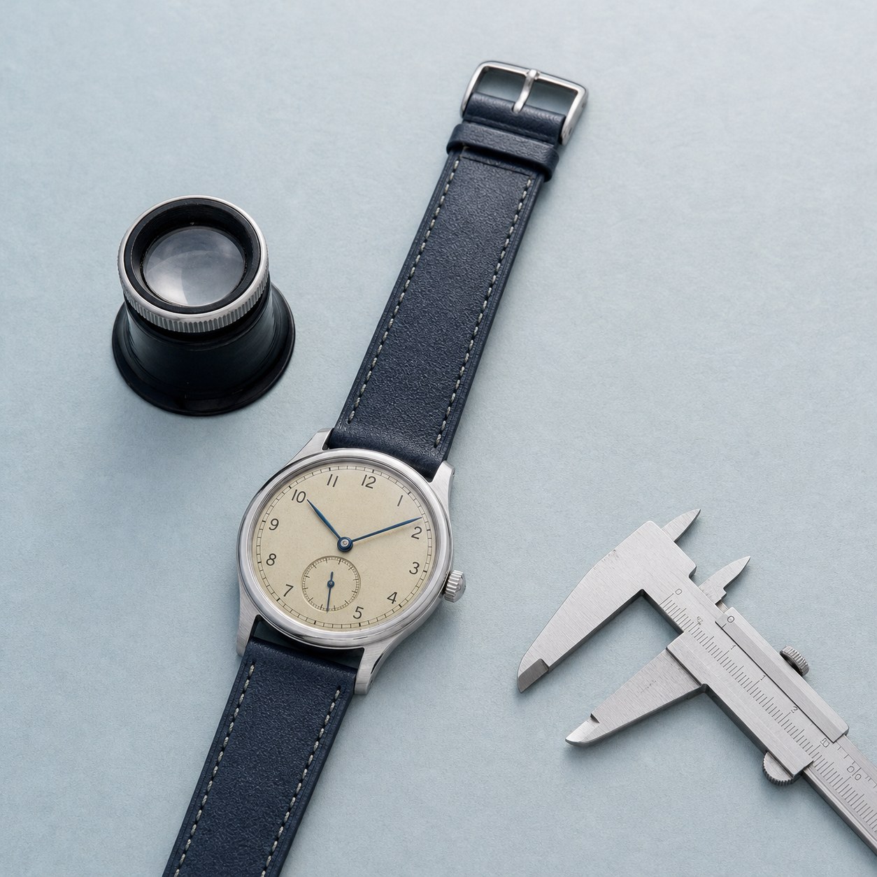 Vintage mechanical wristwatch with a loupe and caliper on a pale blue-grey work surface