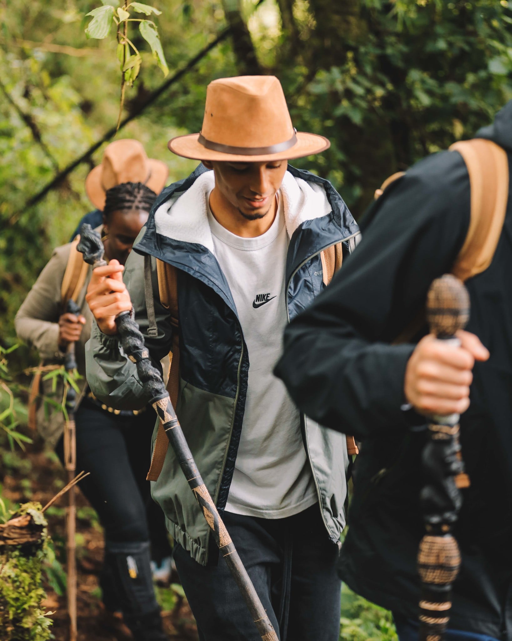A trekker walking through a forest with a hat and walking stick