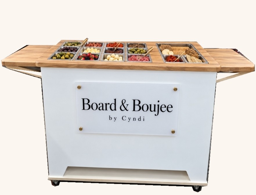 Board & Boujee by Cyndi’s white charcuterie cart with a wooden countertop and individual food compartments