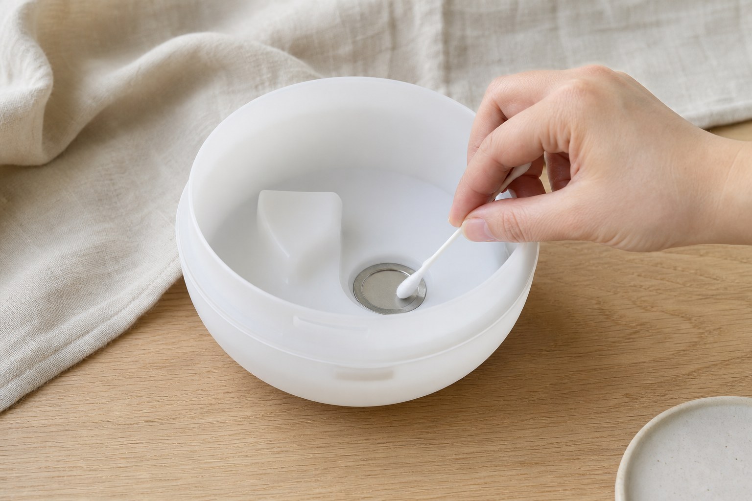 Cotton swab gently cleaning the ultrasonic plate inside an unplugged diffuser reservoir