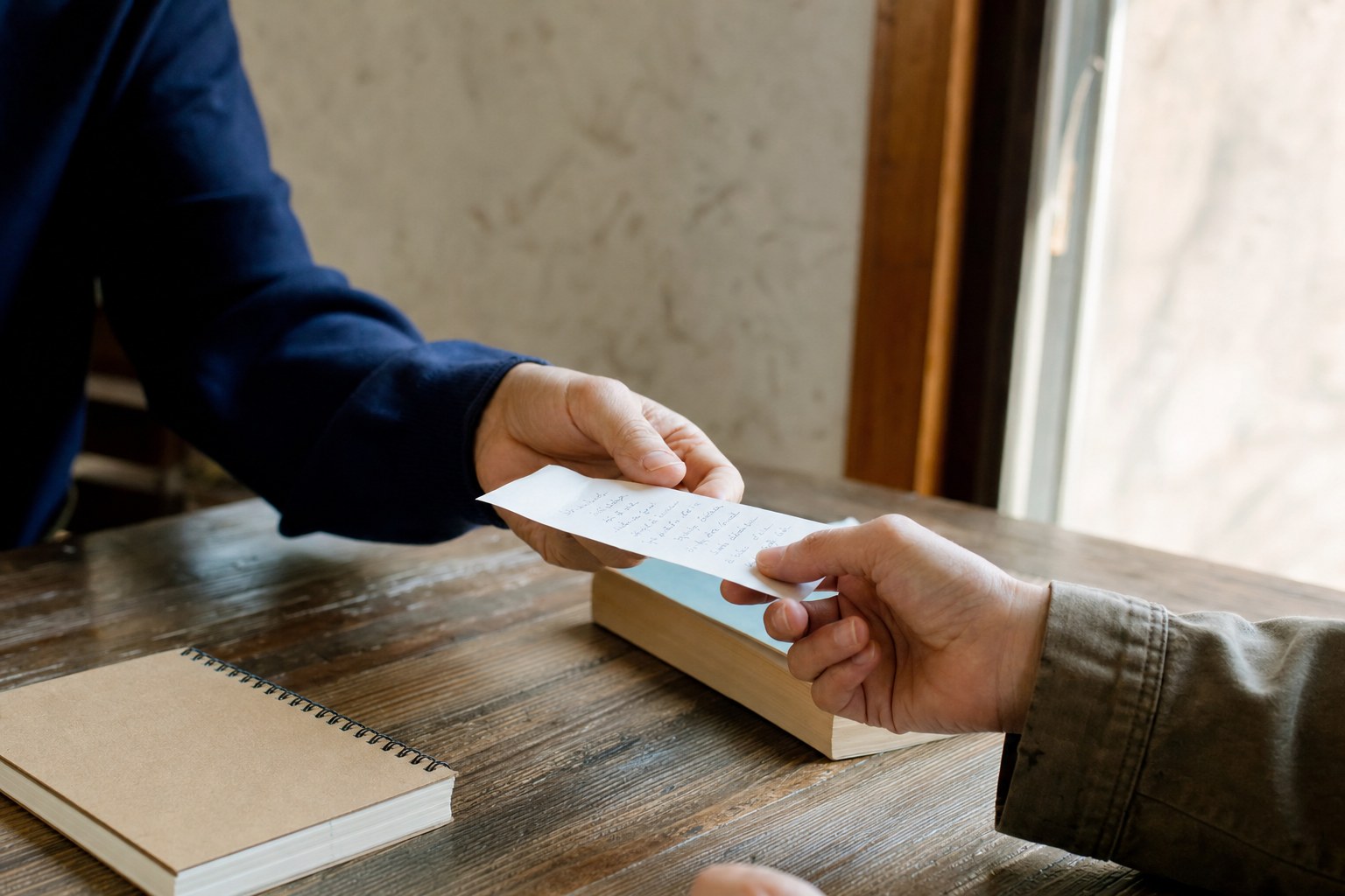 Two people exchanging a handwritten note across a wooden table