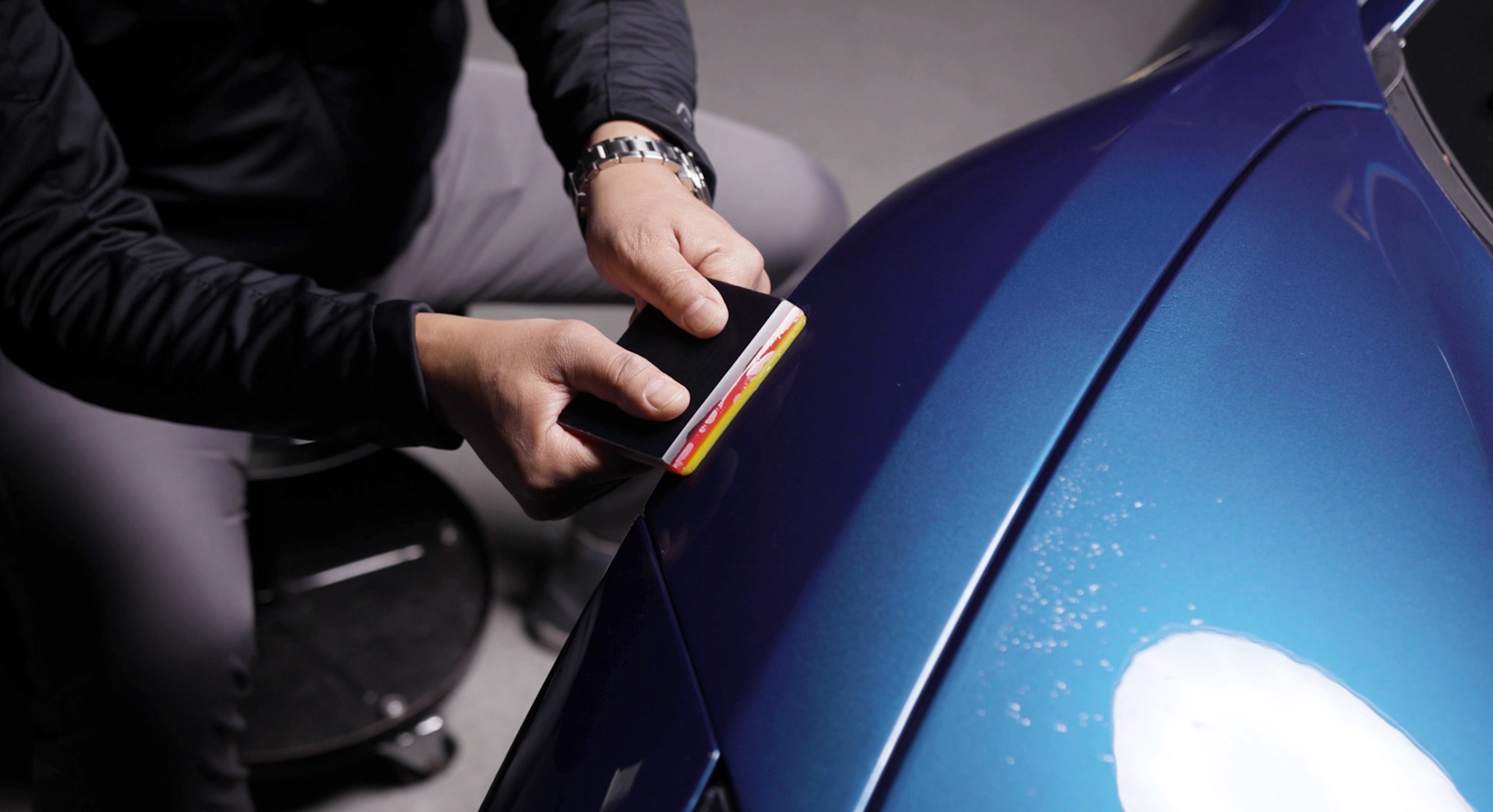 Installer using a squeegee to apply paint protection film to a blue hood