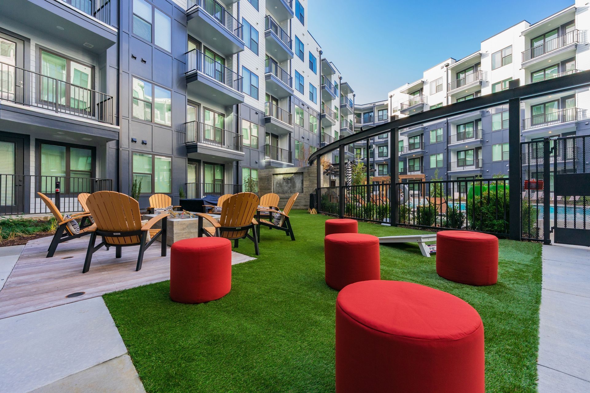 Outdoor lounge area with seating, faux grass, and a pool in a modern apartment complex.