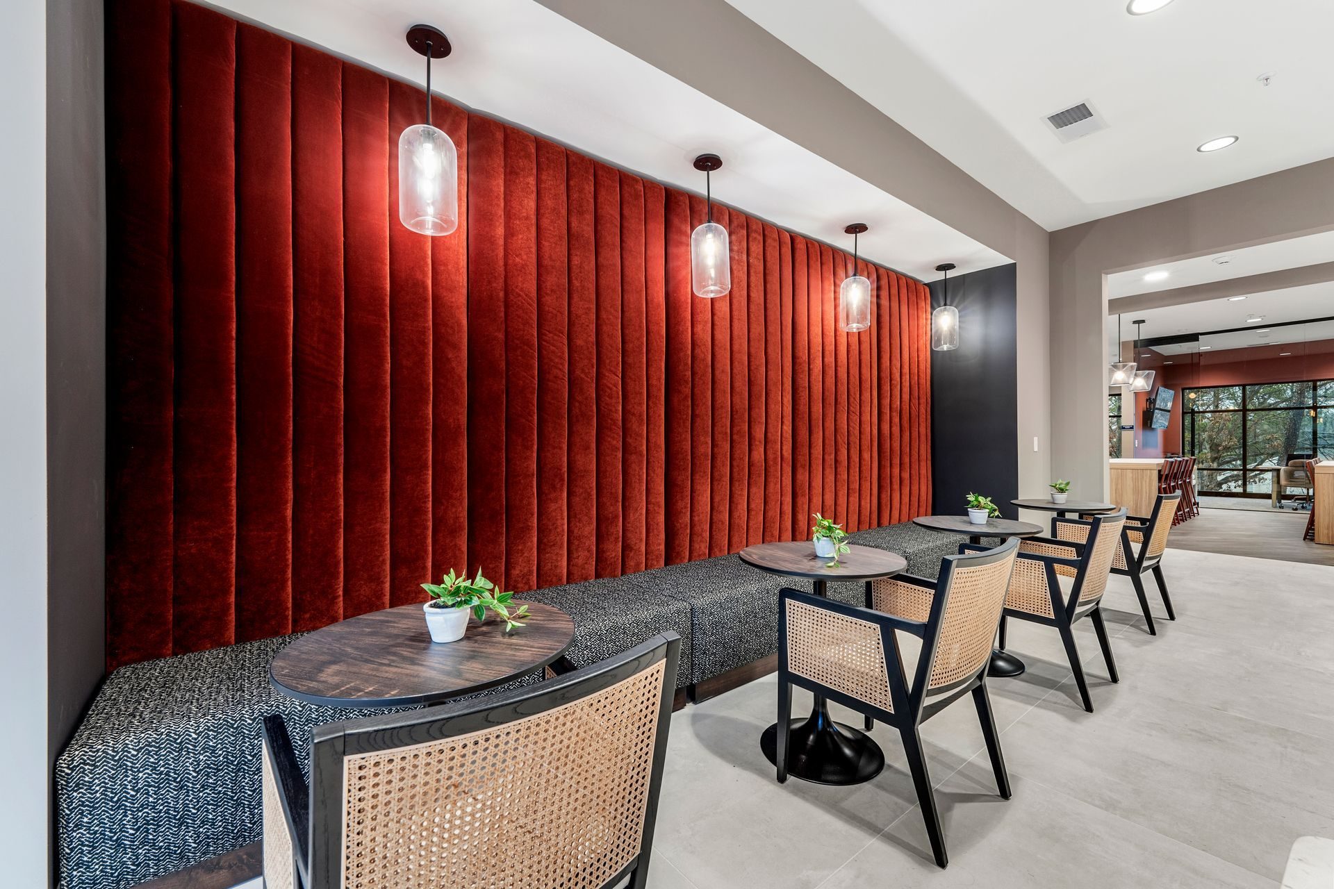 A seating area with a red velvet wall, round tables, black chairs, and pendant lights.