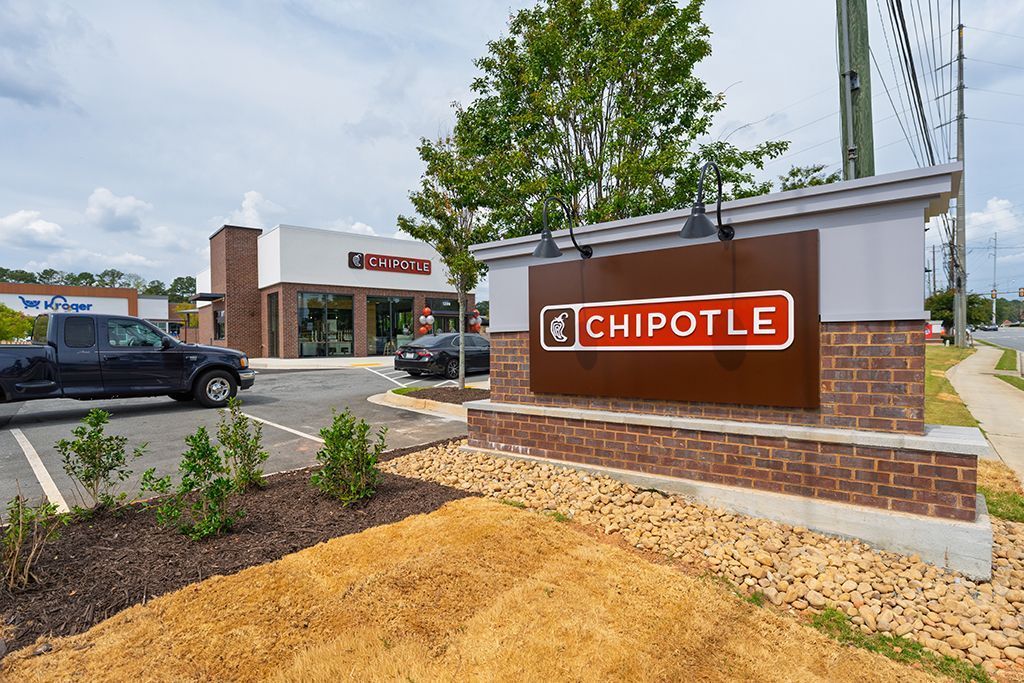 Chipotle restaurant exterior with sign, brick details, parking lot, and a black pickup truck. Cloudy sky.
