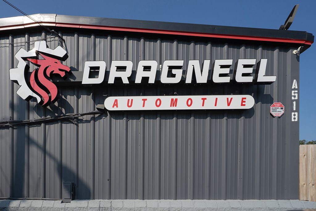 Sign for Dragneel Automotive, featuring a red and white dragon logo and white text on a corrugated metal building.