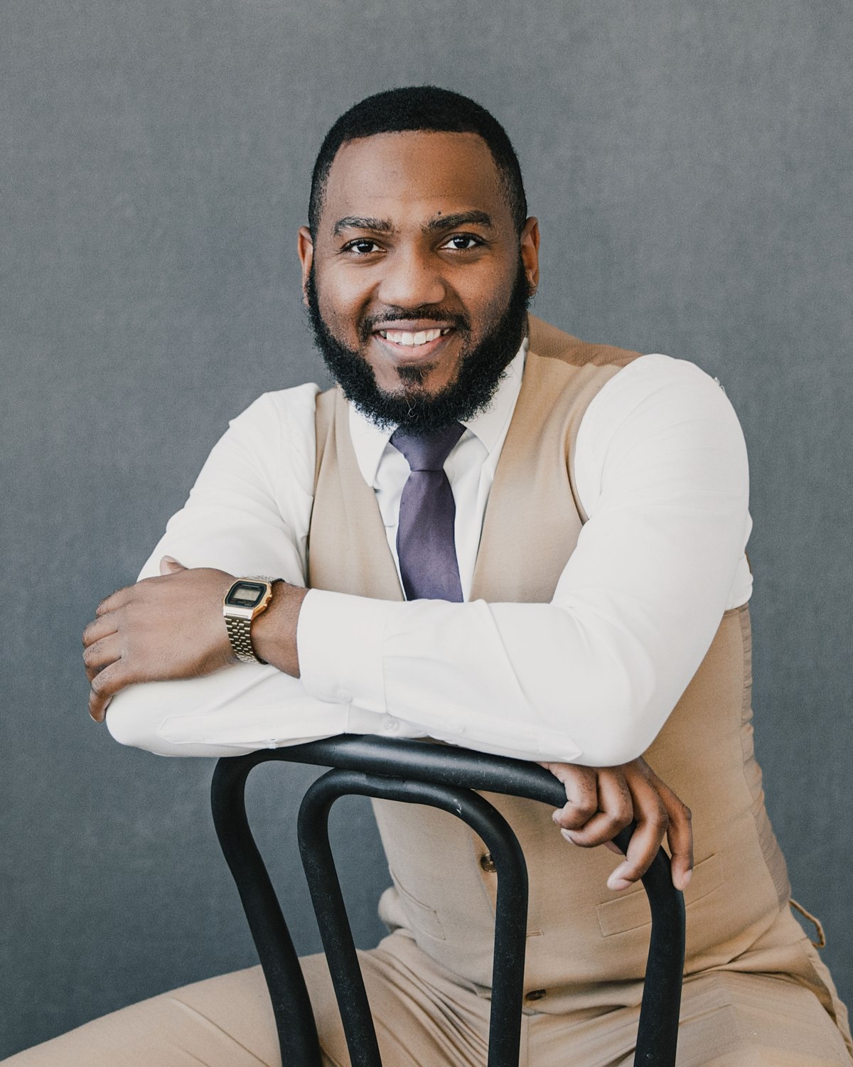 Seated portrait of a smiling man in a tan vest and tie