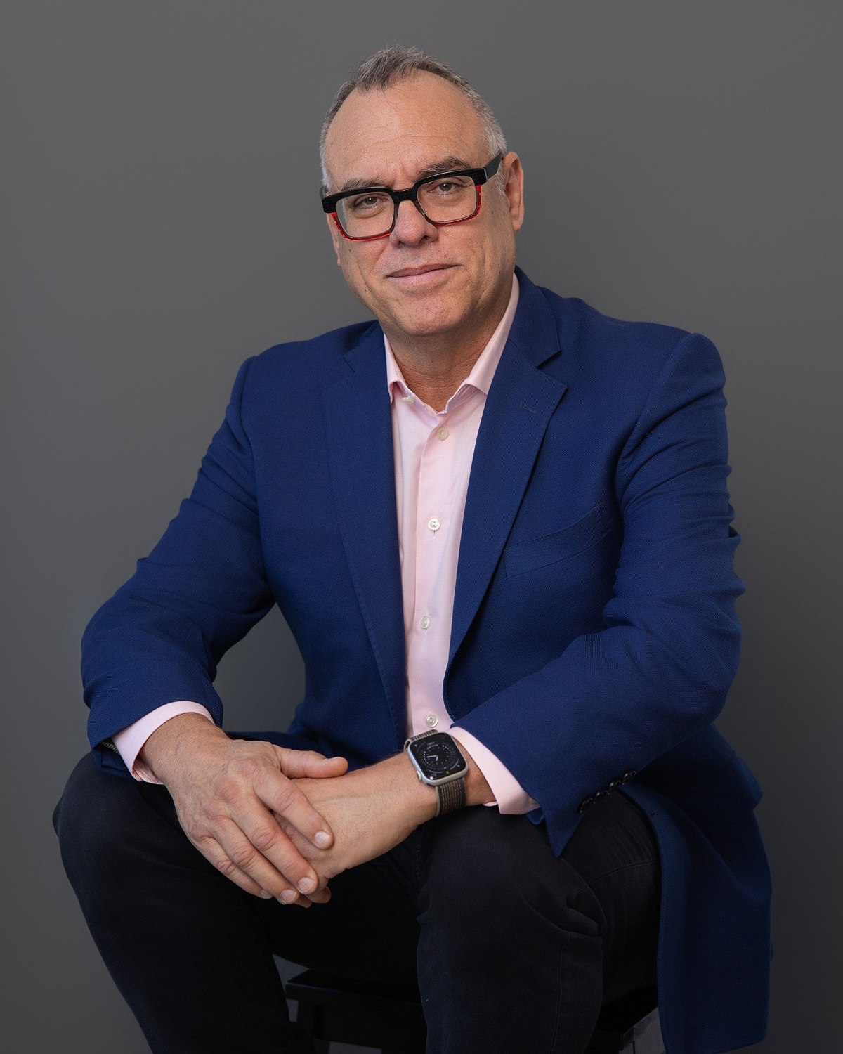 Seated business portrait of a man in glasses and a blue blazer