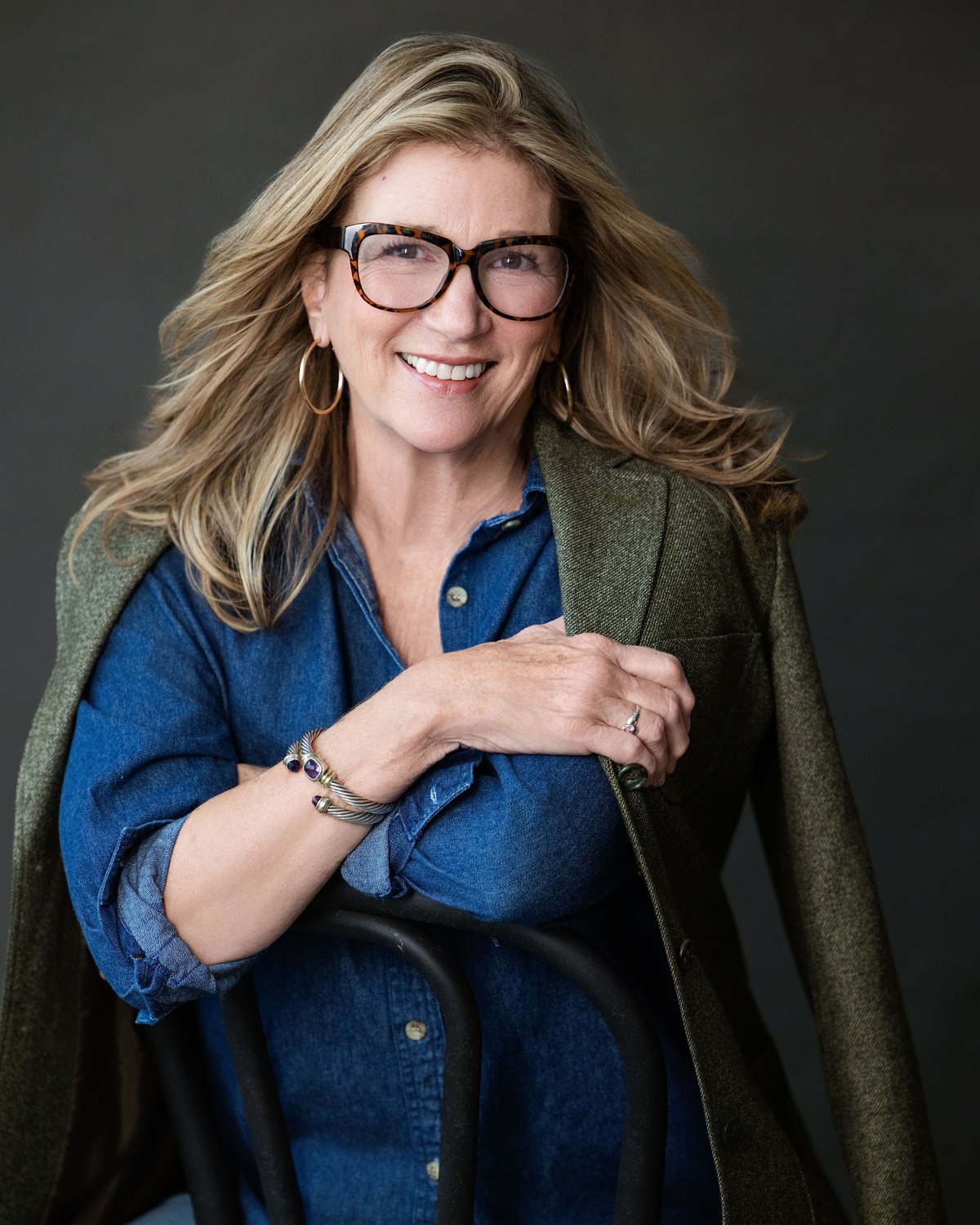 Studio portrait of a smiling woman wearing glasses and a green jacket