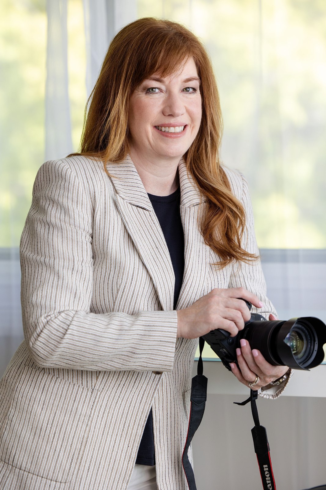 Portrait of a red-haired woman in a light blazer holding a camera