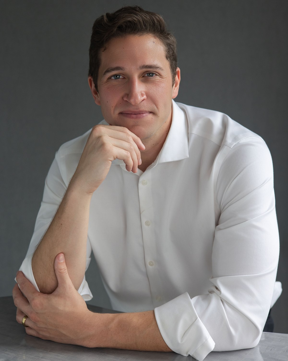 Studio portrait of a man in a white shirt with his hand resting at his chin