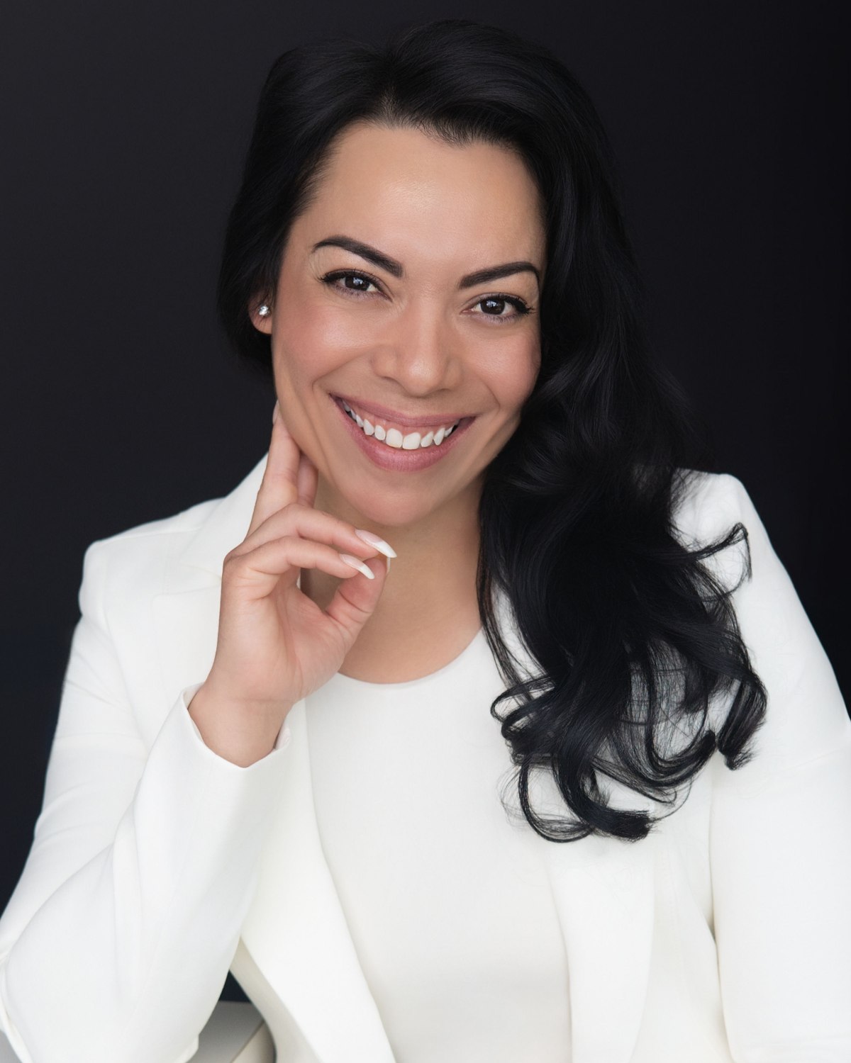 Headshot of a smiling woman in a white blazer against a dark backdrop