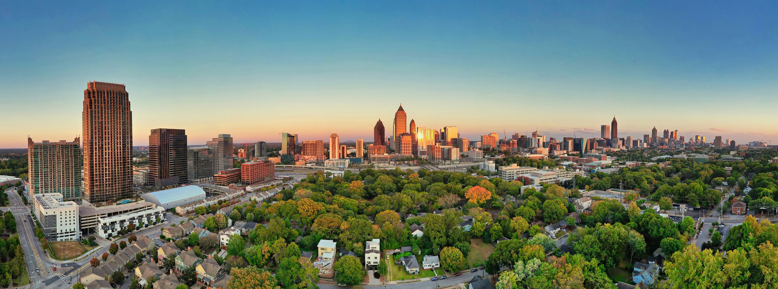 Panoramic Atlanta skyline glowing in sunset light above tree-lined neighborhoods