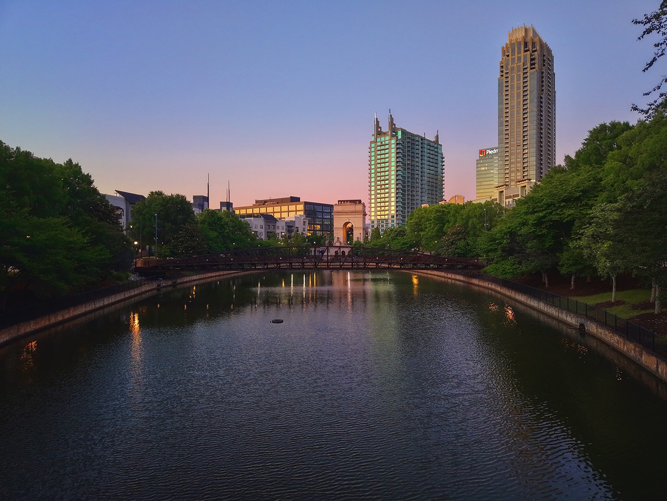 Atlantic Station at dusk with towers, a pedestrian bridge, and reflections across the pond