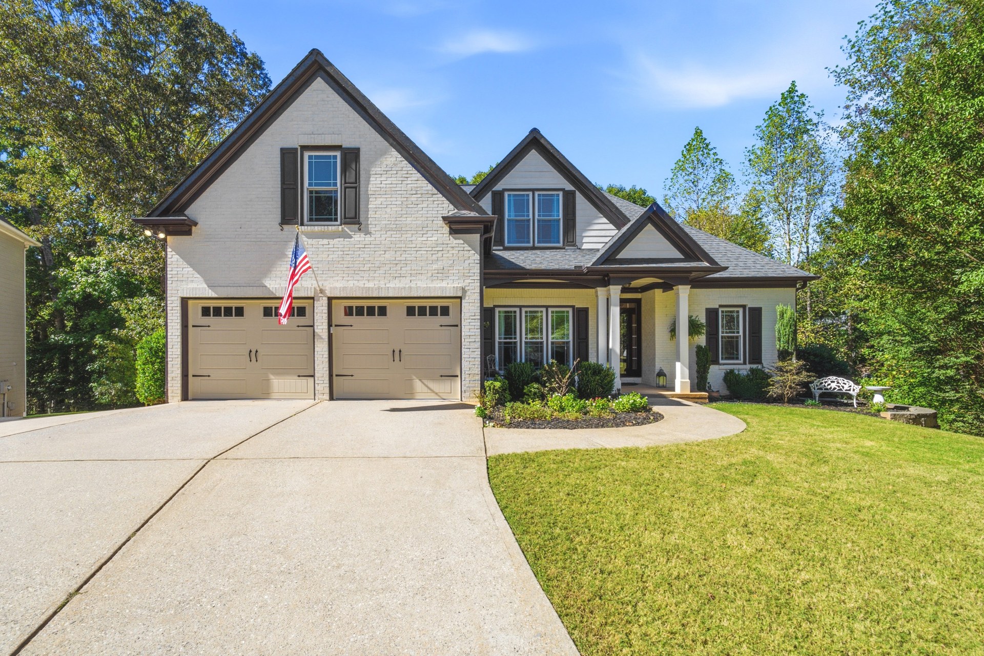 White brick Canton home with dark trim, twin garage doors, a covered front porch, and a tree-lined lawn