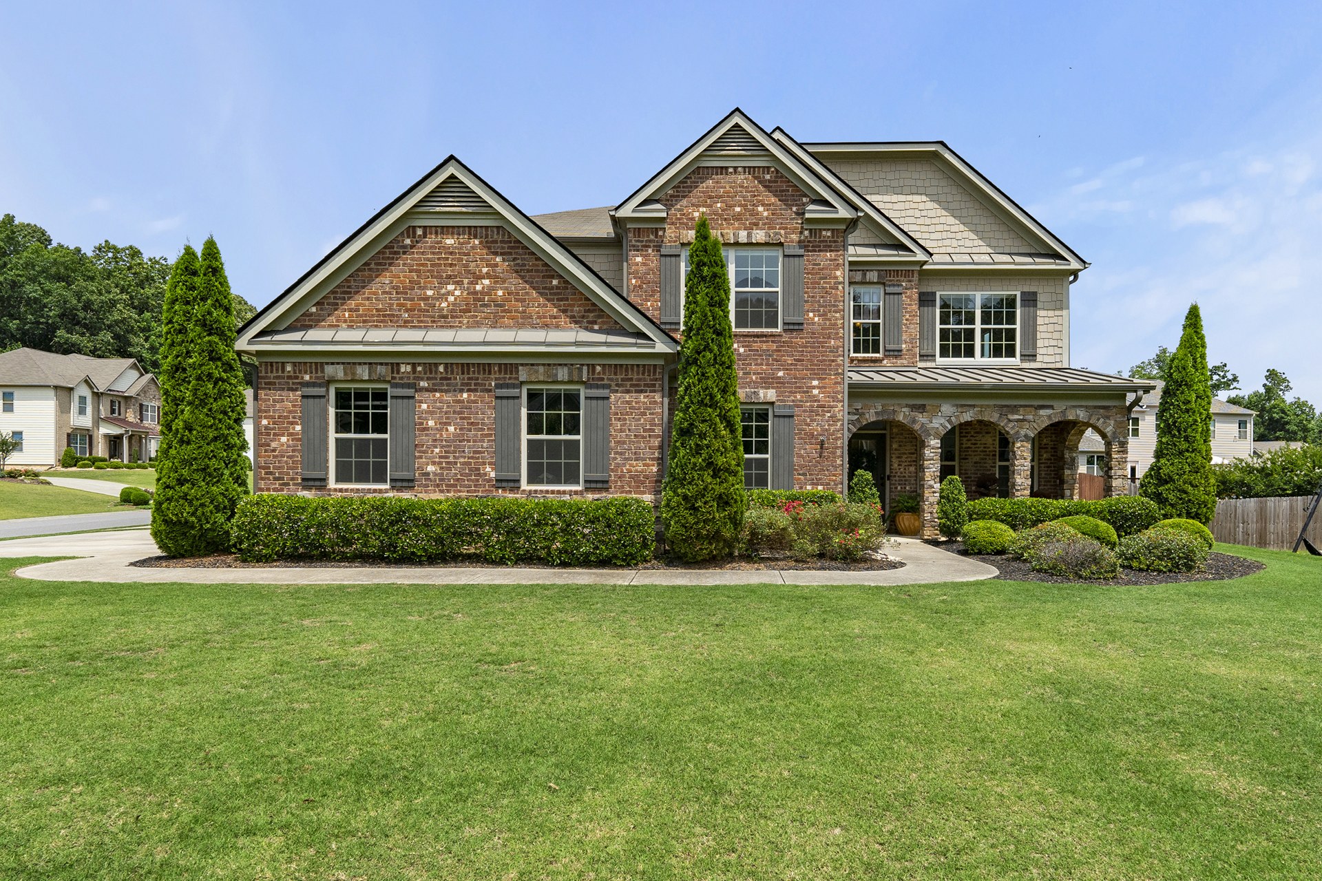 Two-story brick home in Cumming with a stone-arched front porch, tall evergreens, and a broad green lawn