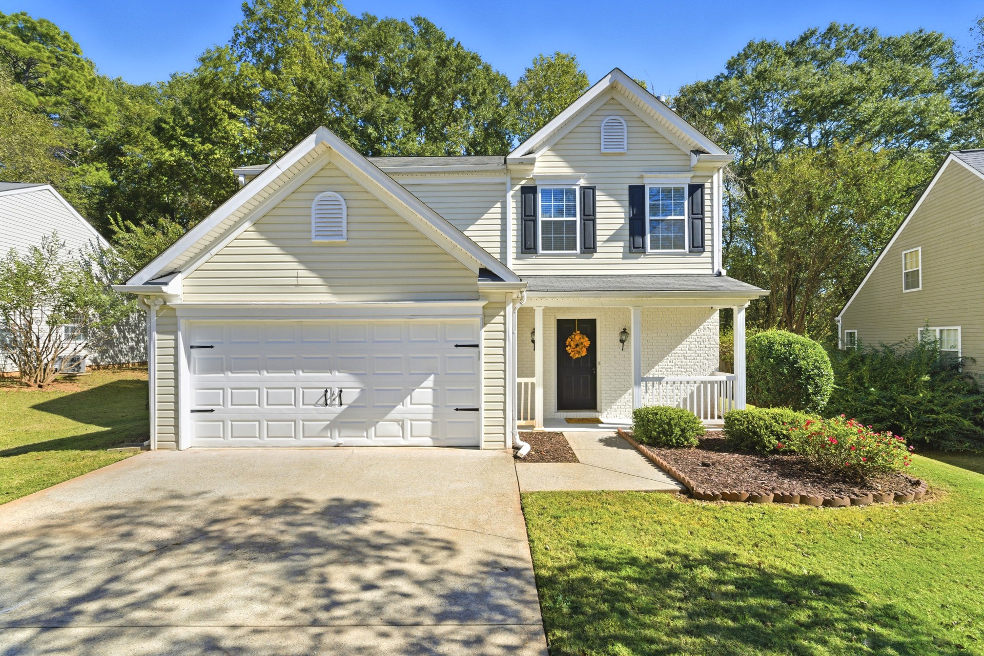 Two-story Holly Springs home with cream siding, black shutters, a white front porch, and a landscaped lawn