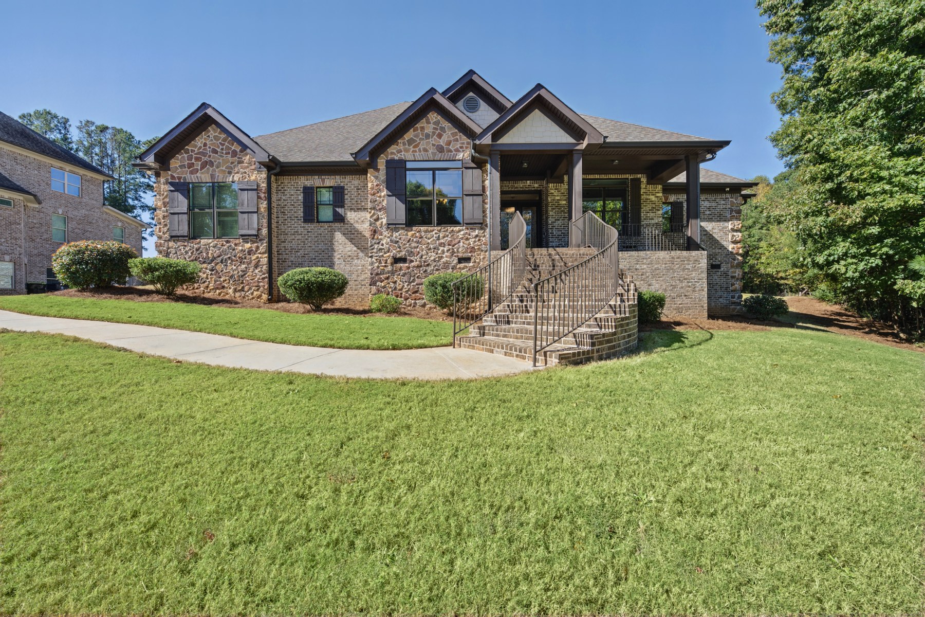 Stone and brick home with a covered front porch, curved entry steps, and a green lawn