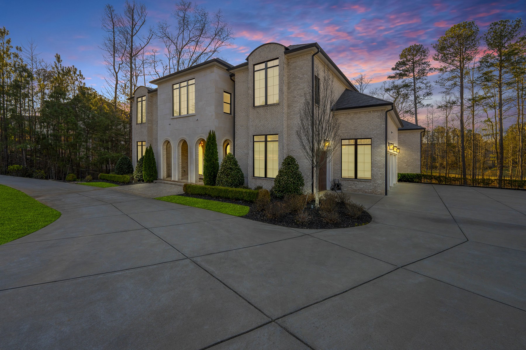 Light brick home at twilight with tall windows, arched entryways, and a sweeping driveway