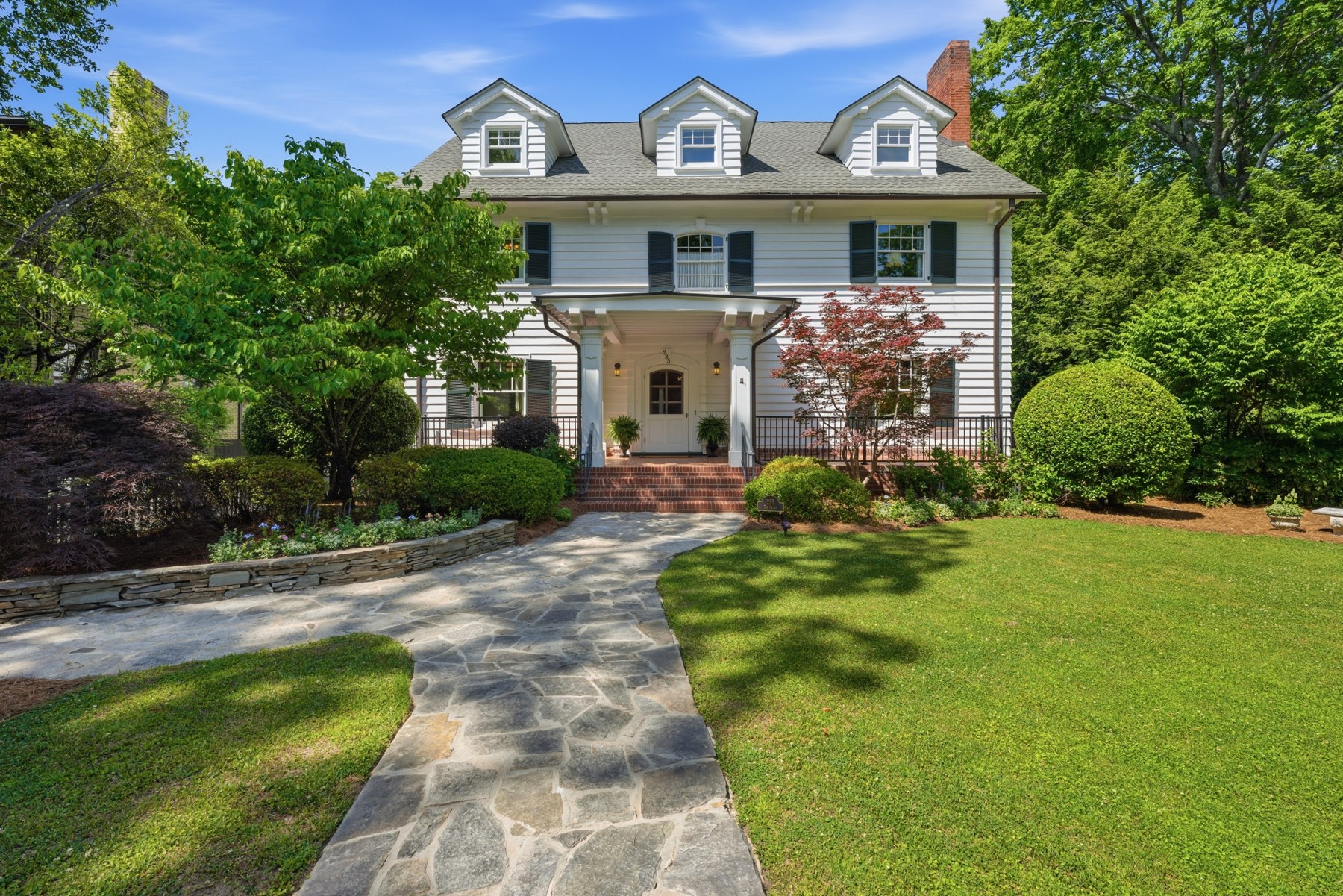 White two-story home with dormer windows, a covered entry, and a landscaped front yard