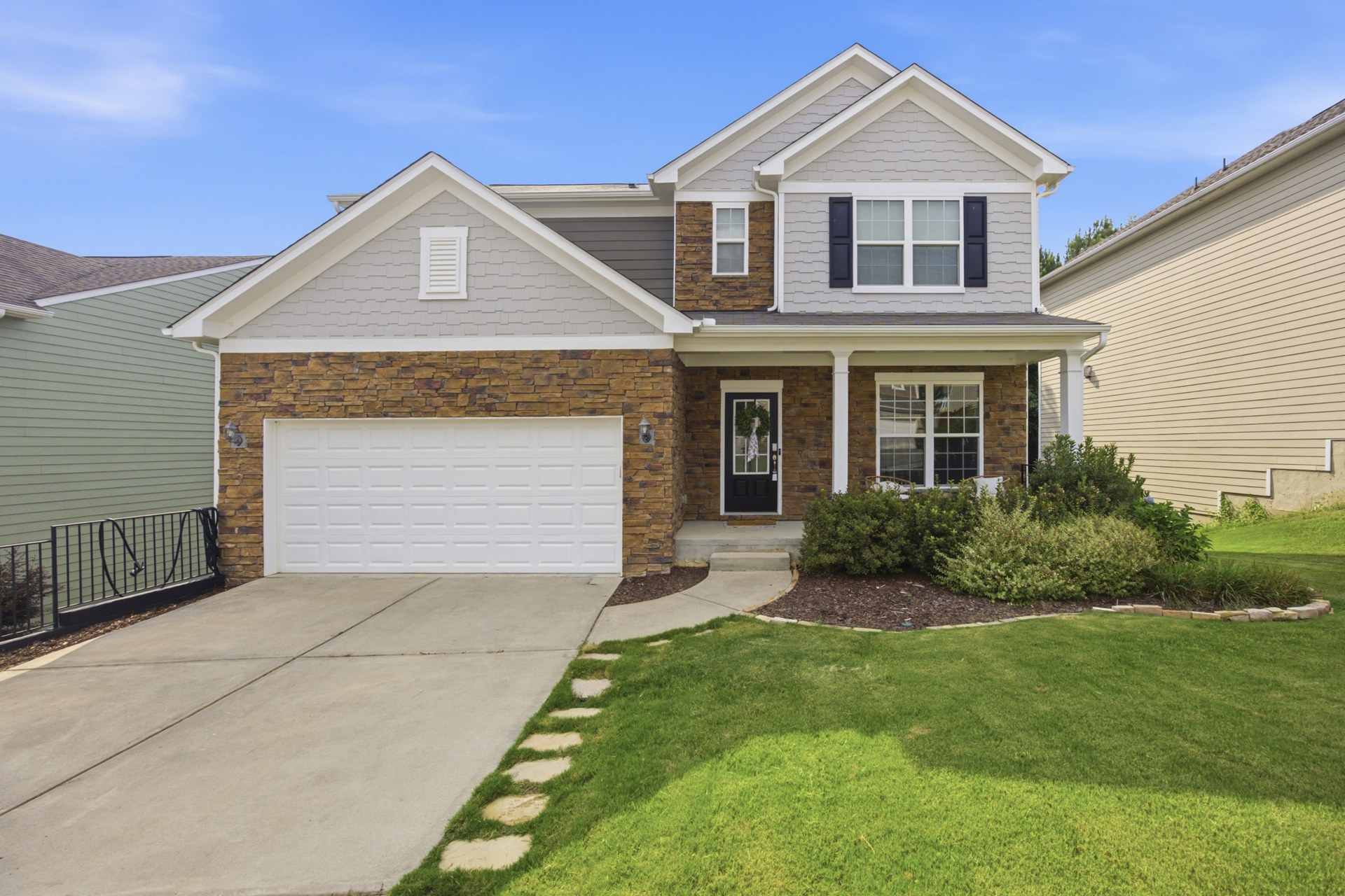 Two-story Sugar Hill home with a stone facade, white trim, covered front porch, and green lawn