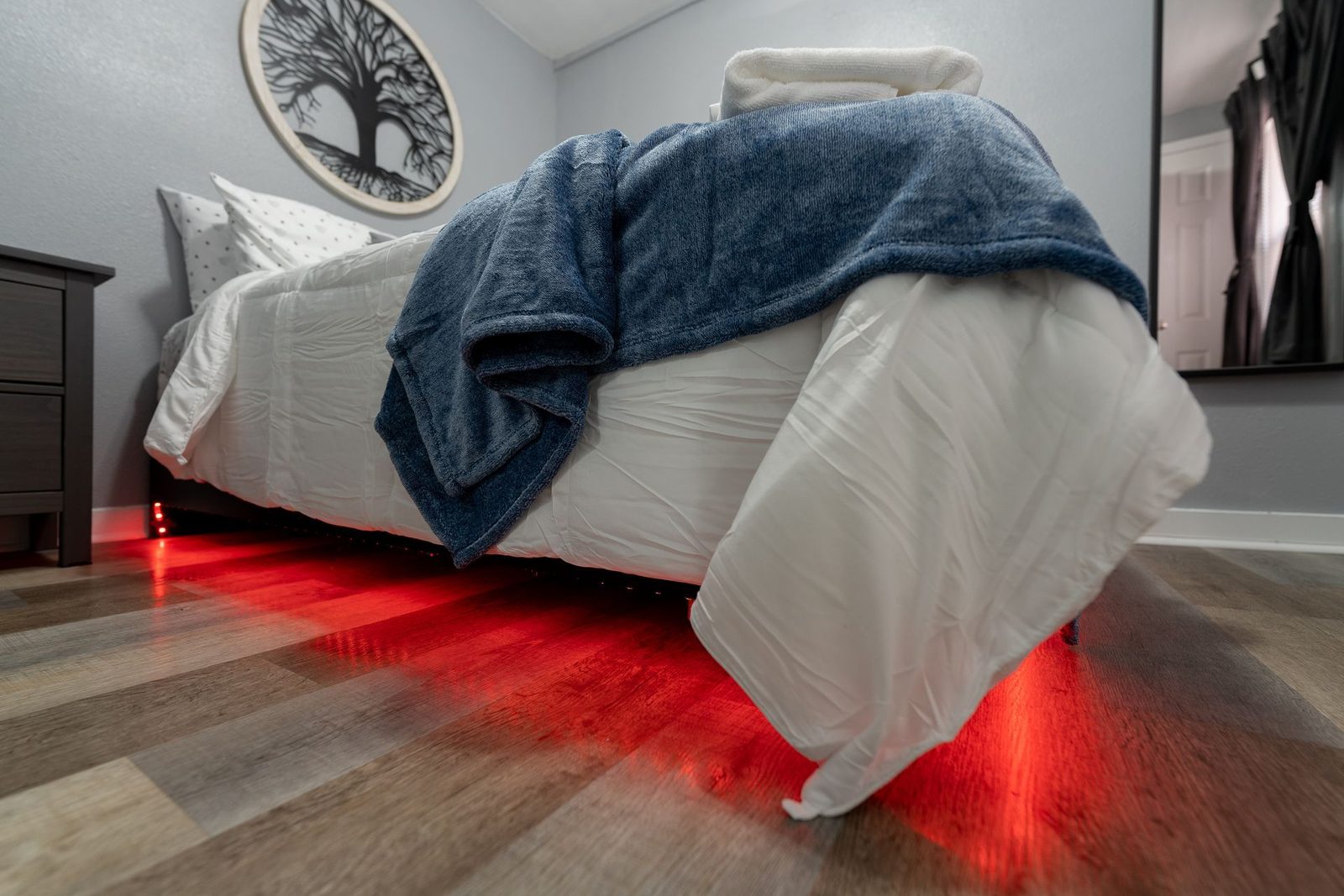 A bed in a bedroom with red lights underneath it.