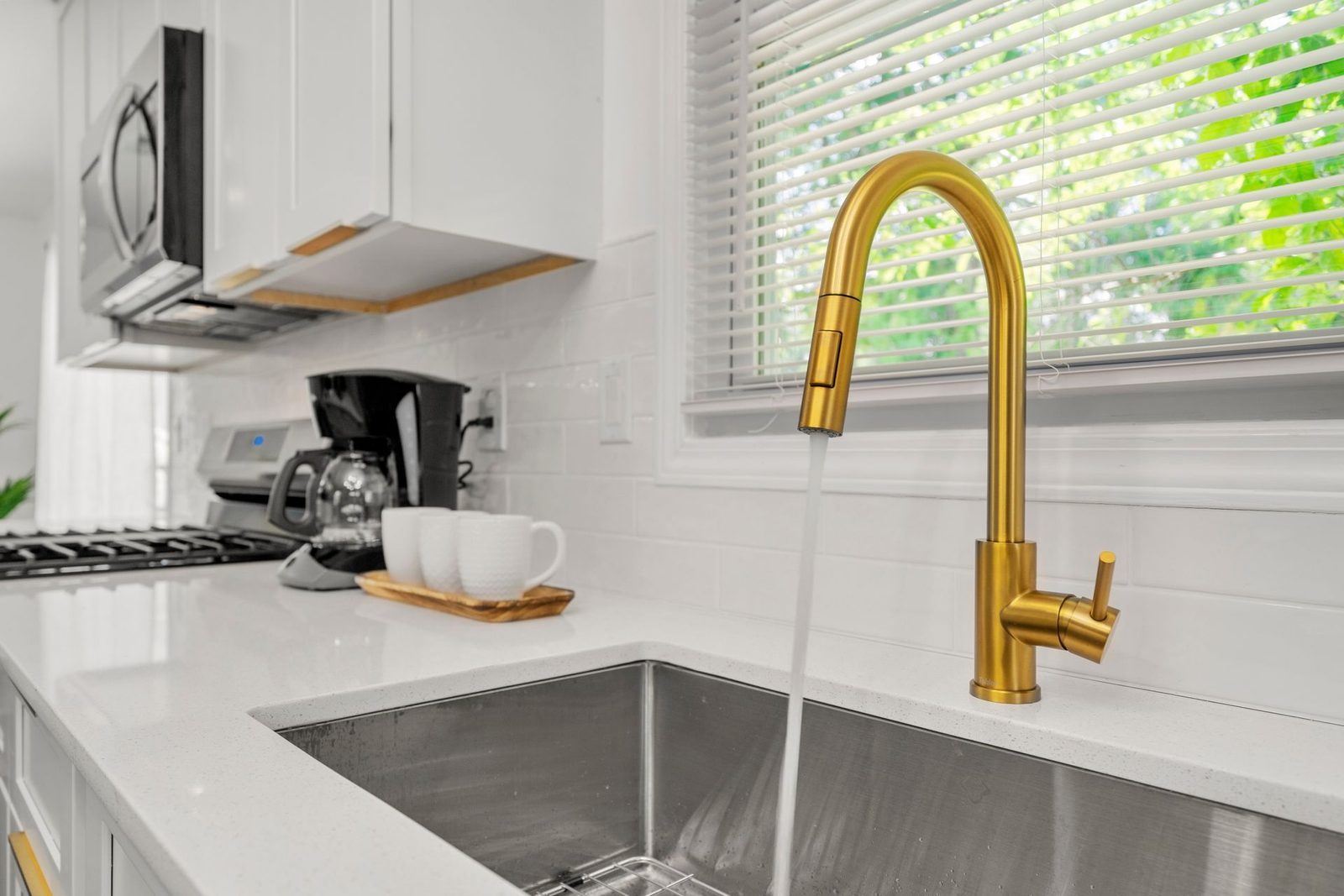 A kitchen sink with a gold faucet and water running out of it.