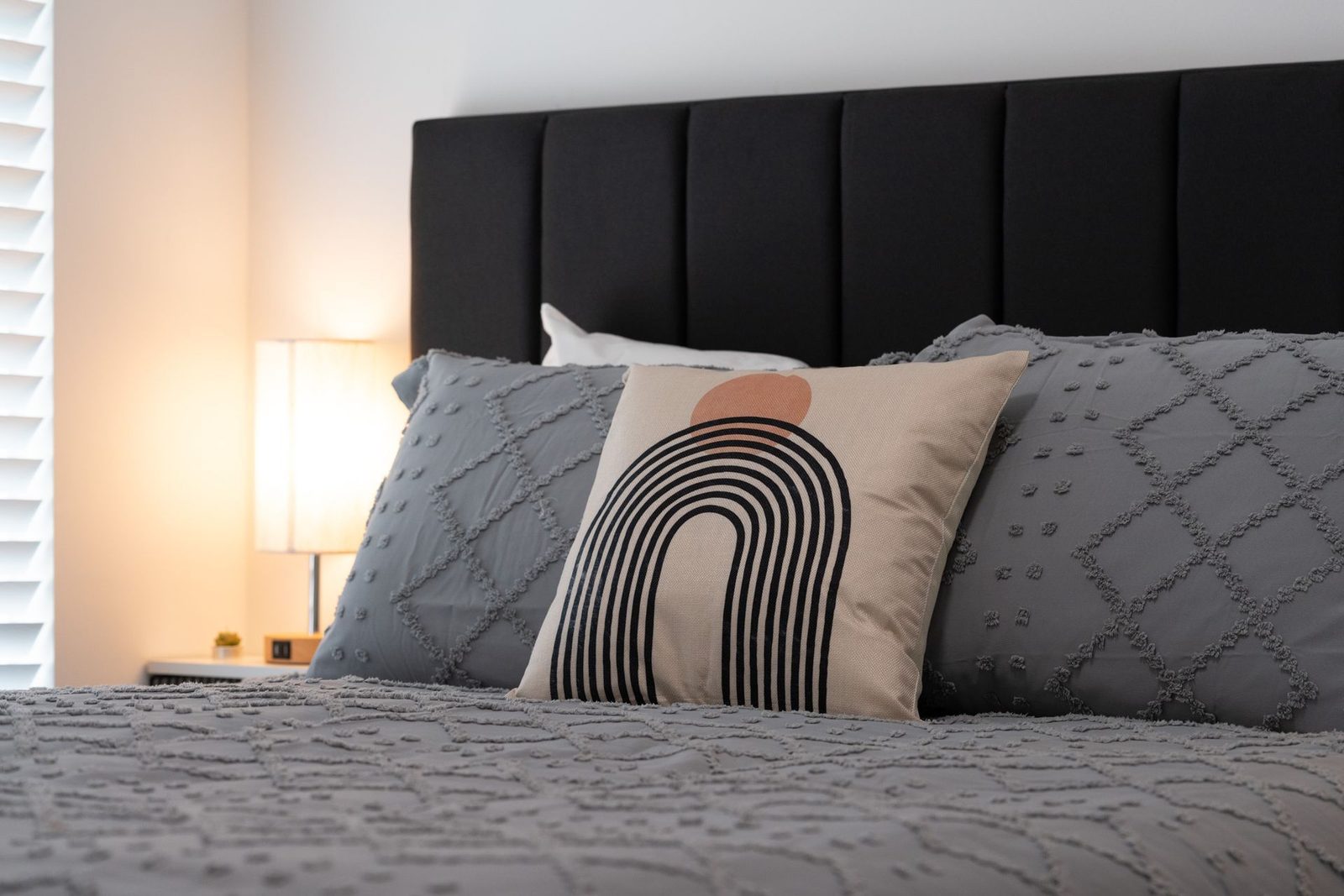 A bed with a black headboard and a rainbow pillow on it.