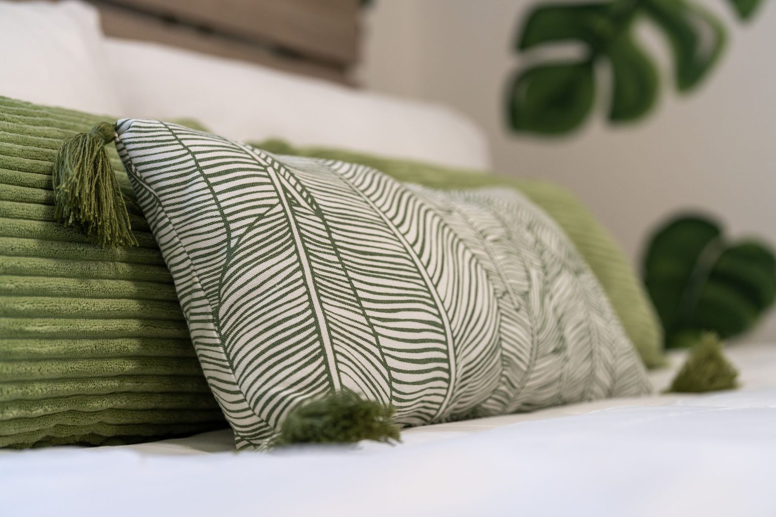 A bed with green pillows and a plant in the background.