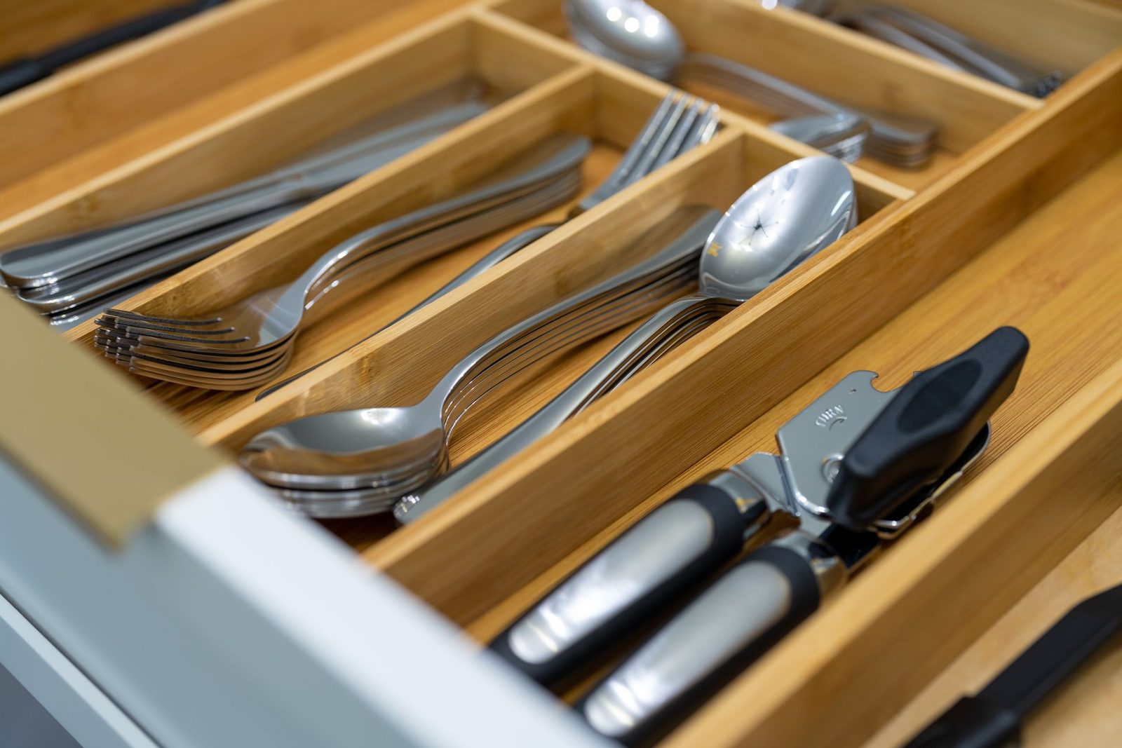A wooden drawer filled with silverware and a can opener.