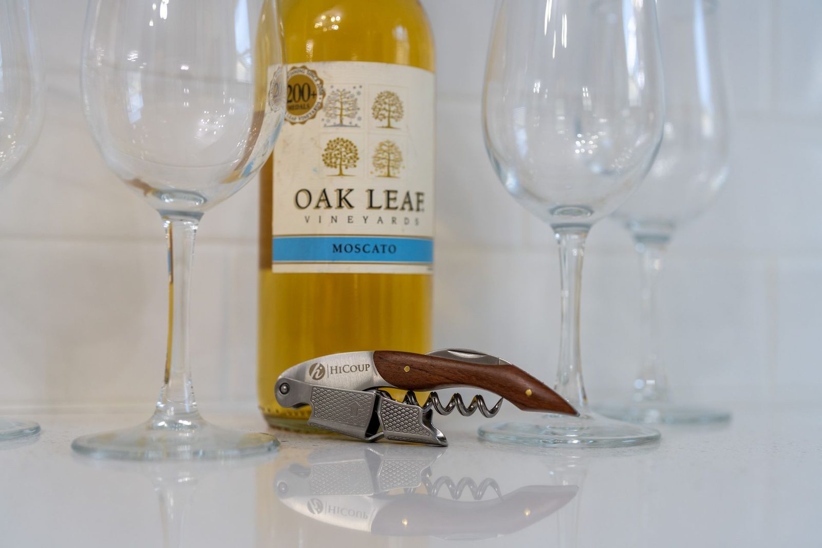 A bottle of oak leaf wine is next to empty wine glasses and a corkscrew.