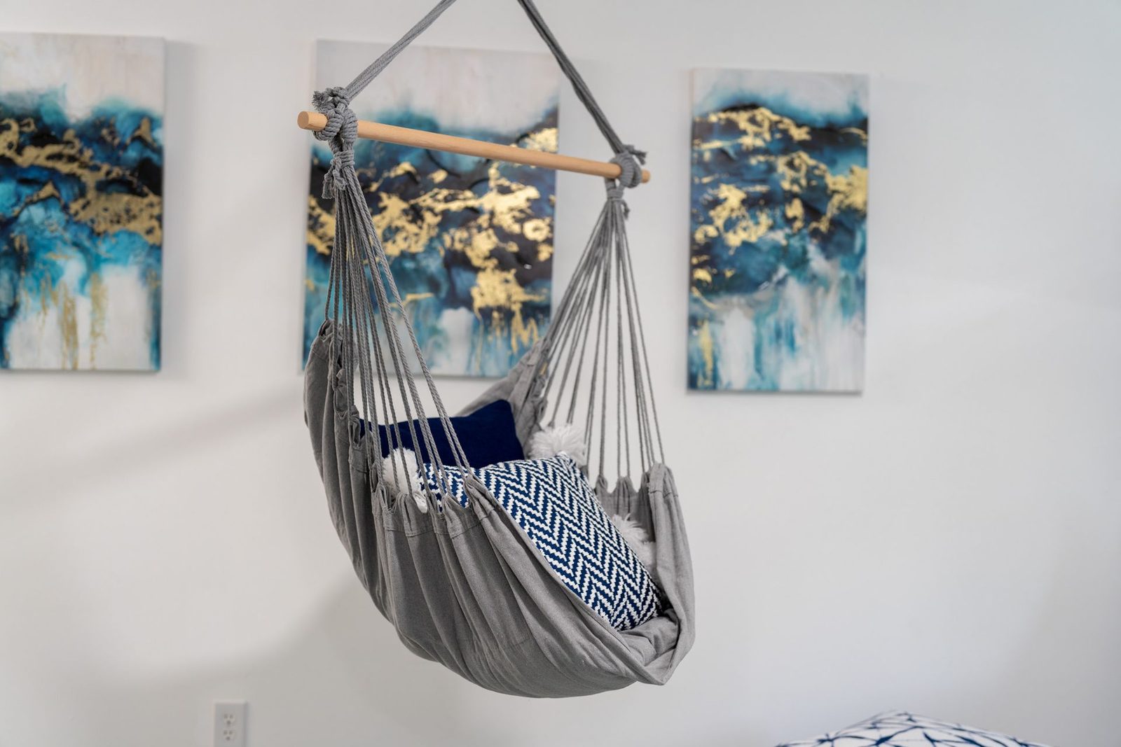 A hammock is hanging from the ceiling in a room with three paintings on the wall.