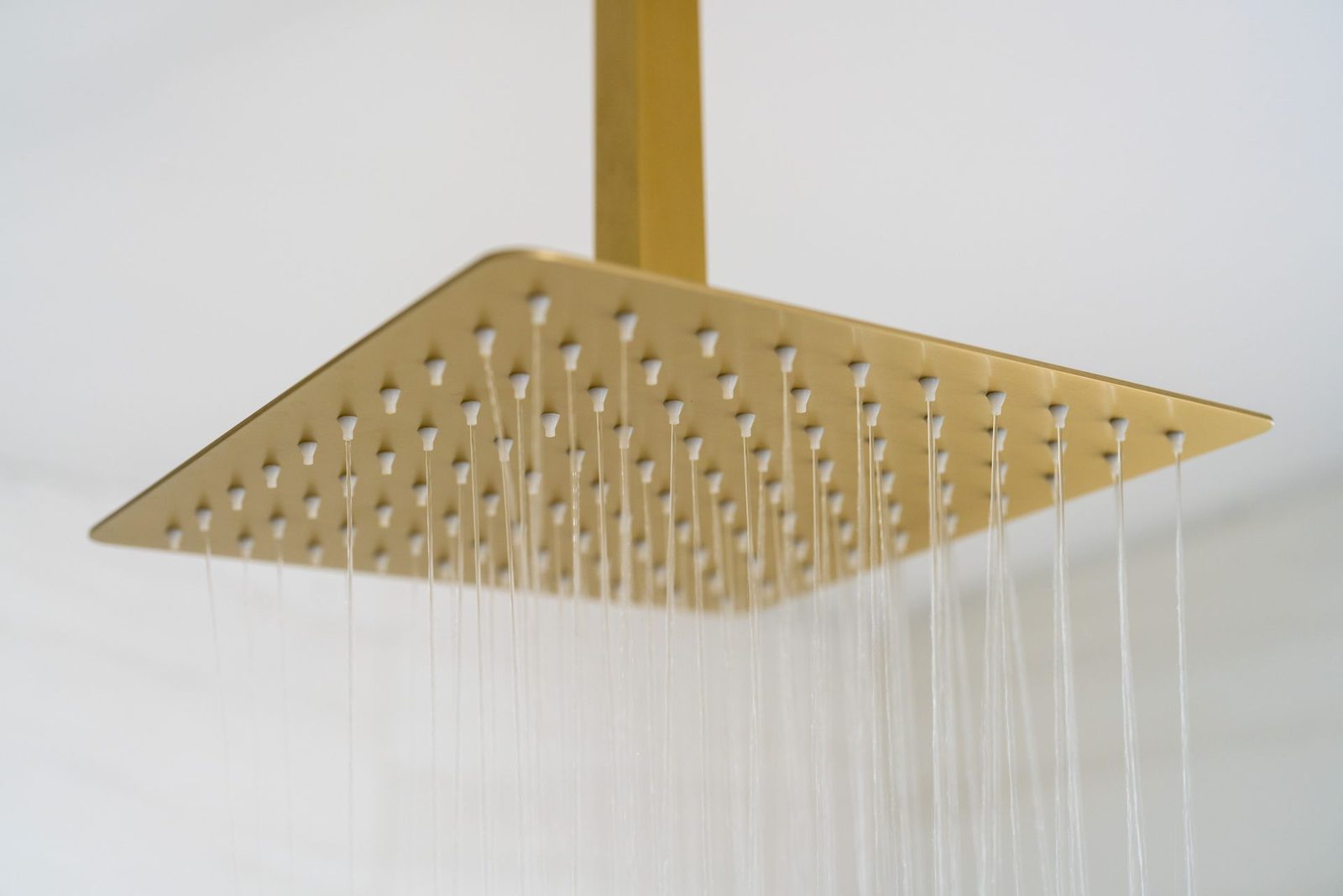 A square shower head is hanging from the ceiling in a bathroom.