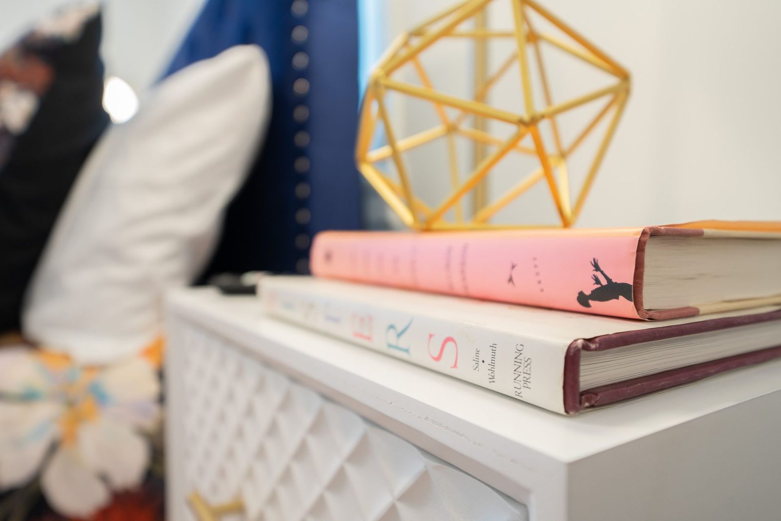 Two books are stacked on top of each other on a nightstand.