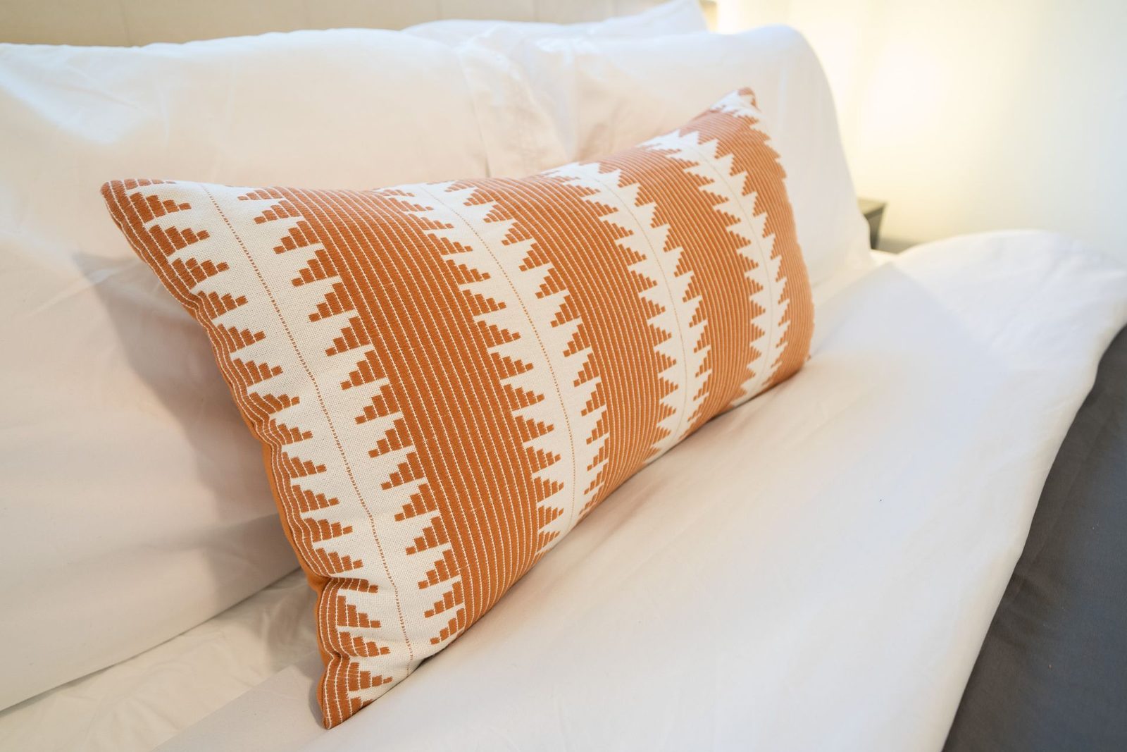 An orange and white pillow is sitting on a bed.