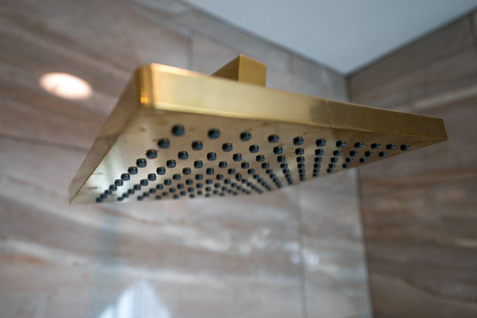 A gold shower head is hanging from the ceiling in a bathroom.