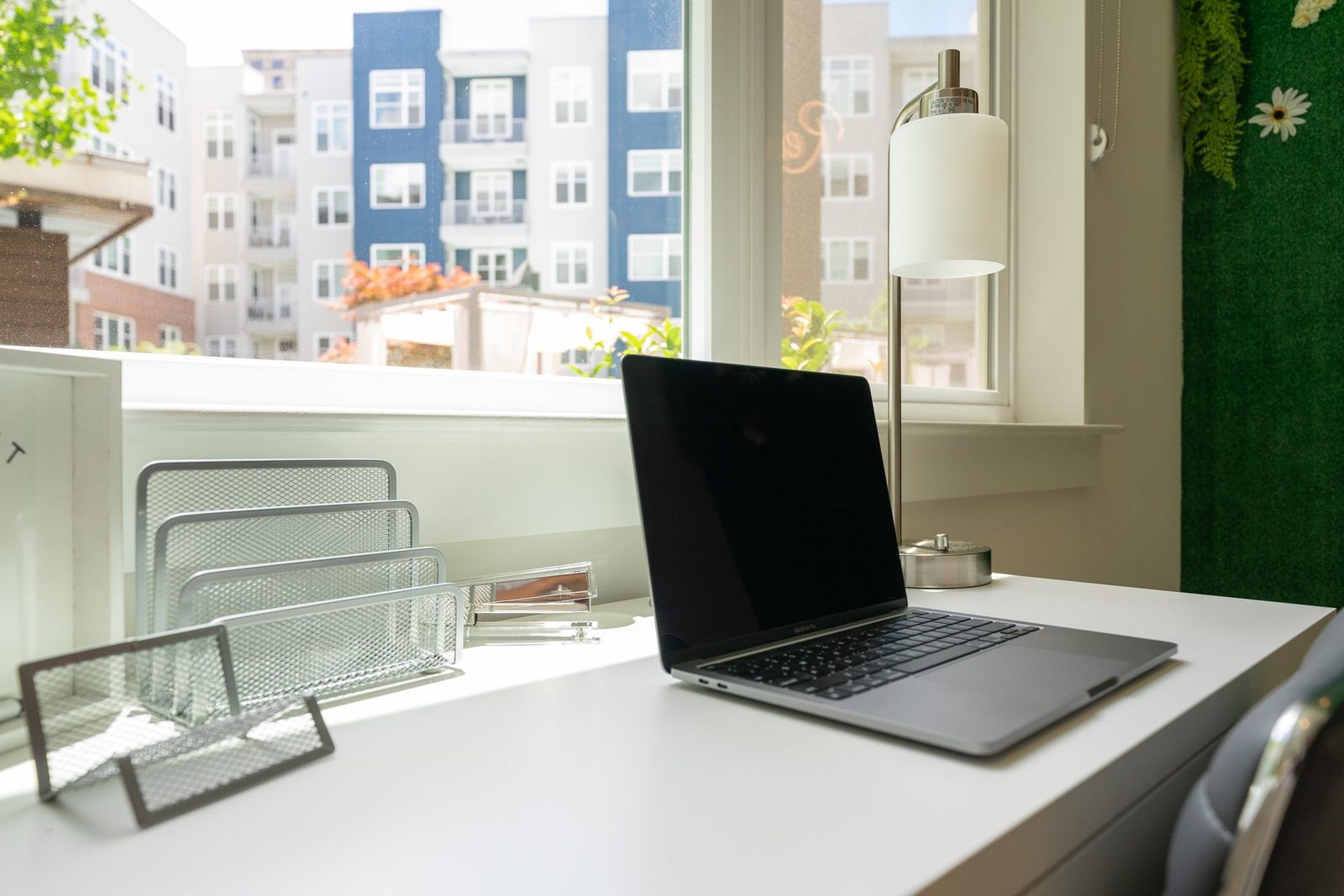A laptop computer is sitting on a white desk in front of a window.