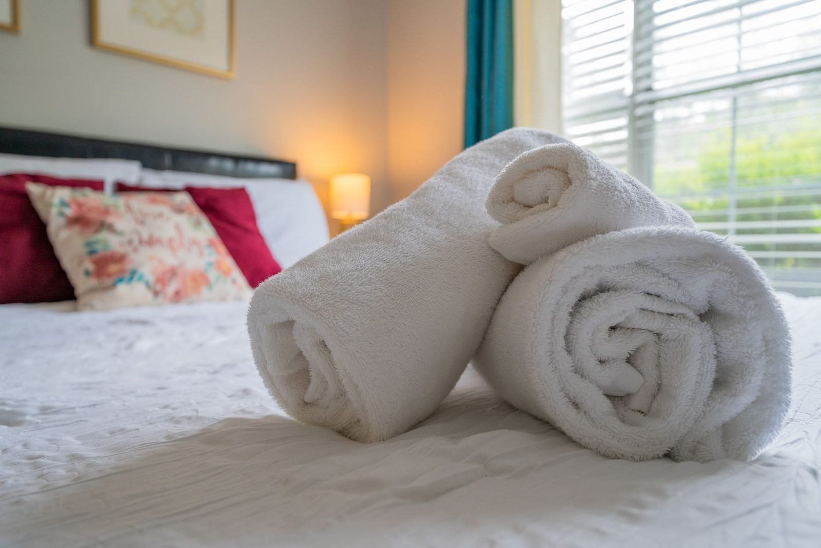 Two towels are rolled up on a bed in a bedroom.