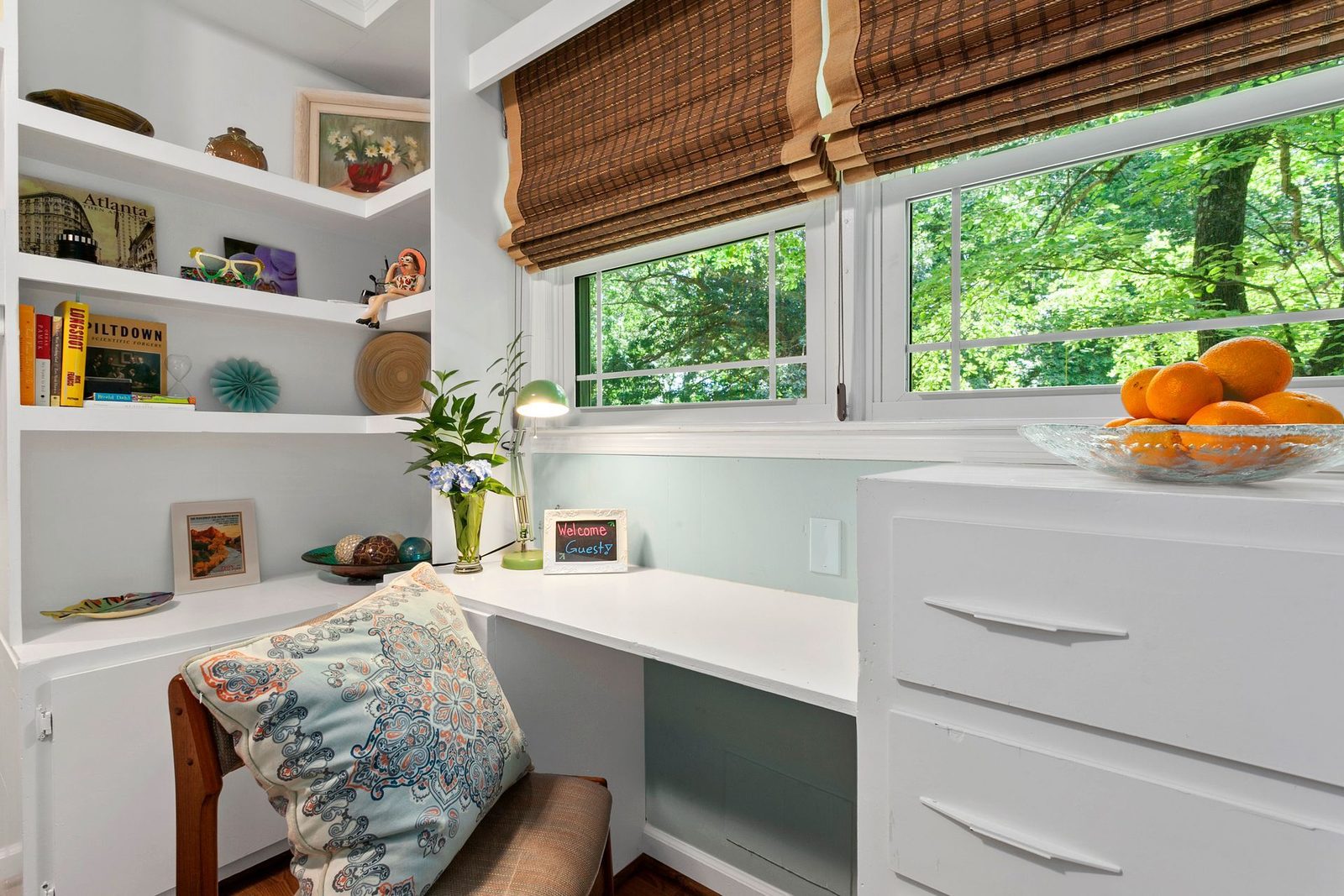 A room with a desk and a bowl of oranges on the counter