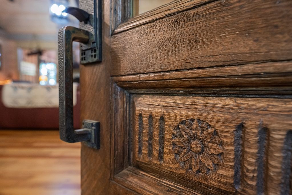 Close-up of a detailed wooden door with an ornate handle, partially open revealing a room.
