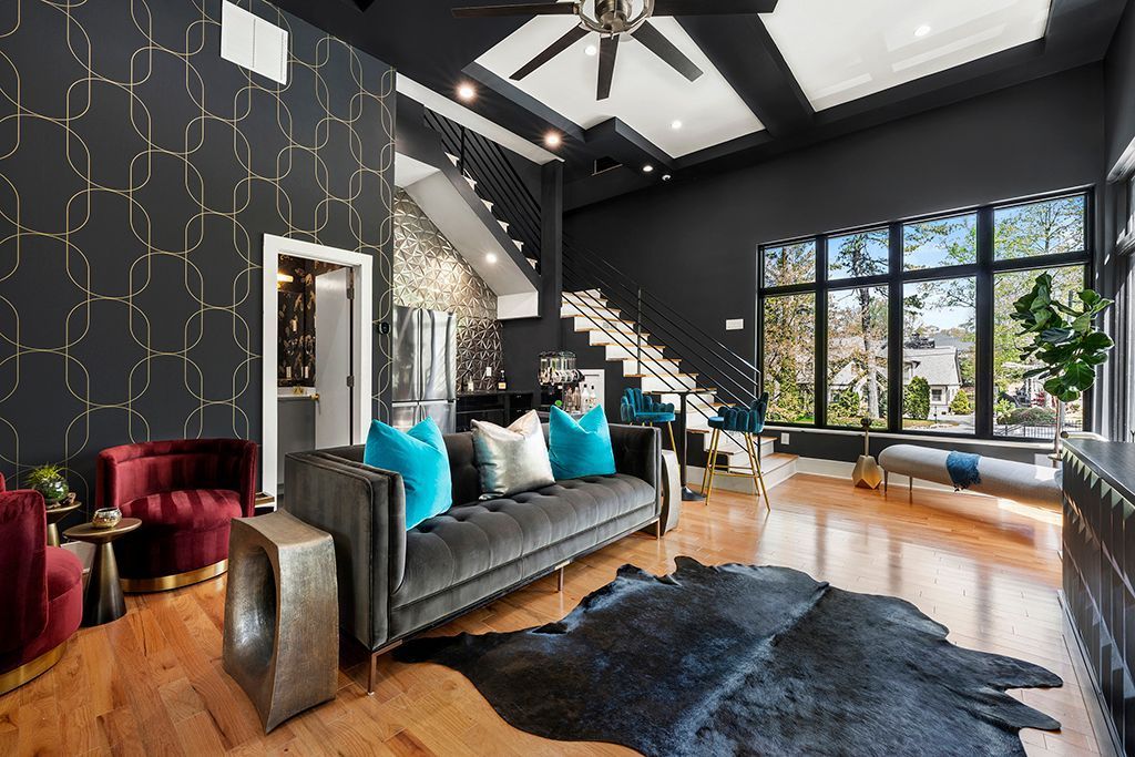 Living room with dark gray walls, velvet sofa, turquoise pillows, a black cowhide rug, and gold geometric wallpaper.