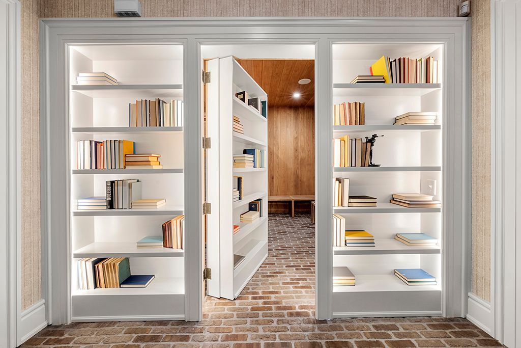 Built-in white bookshelves flanking a doorway leading to a hidden room. Books and objects are on the shelves.