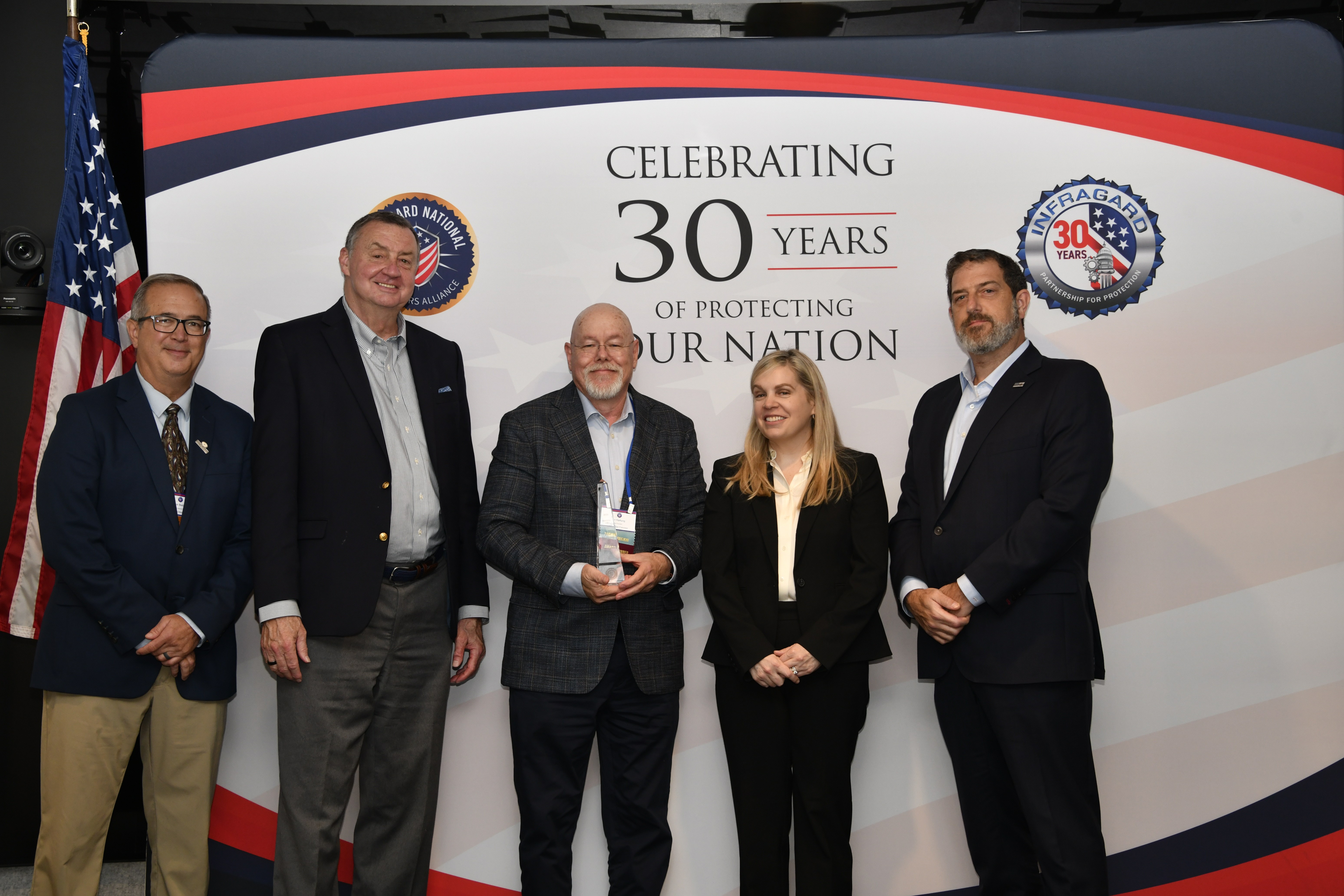 Don Hartung holding his Meeting the Challenge Award with fellow attendees at InfraGard’s 30th anniversary celebration