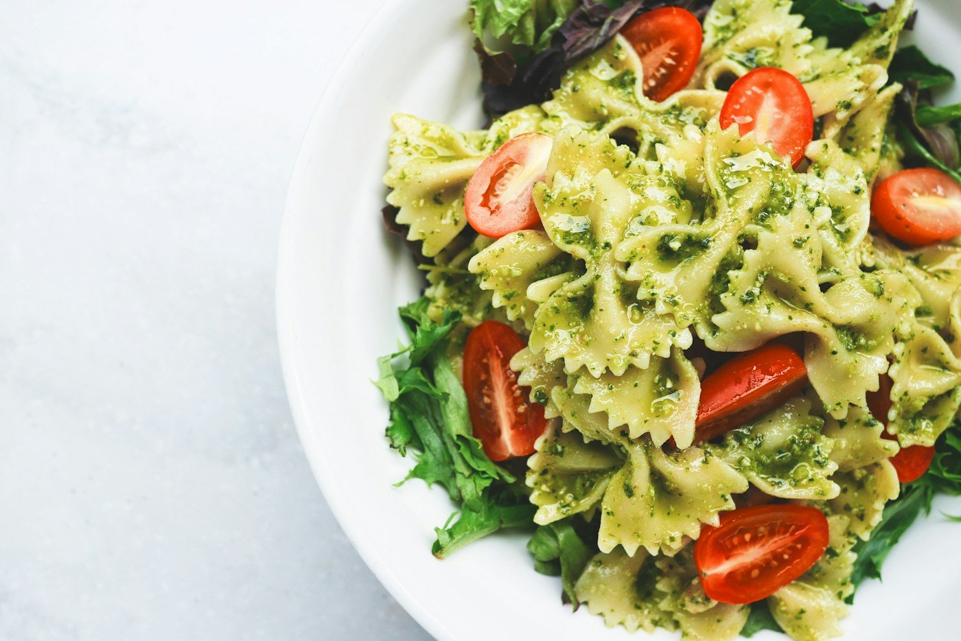 Farfalle pasta with green sauce, tomatoes, and leafy greens