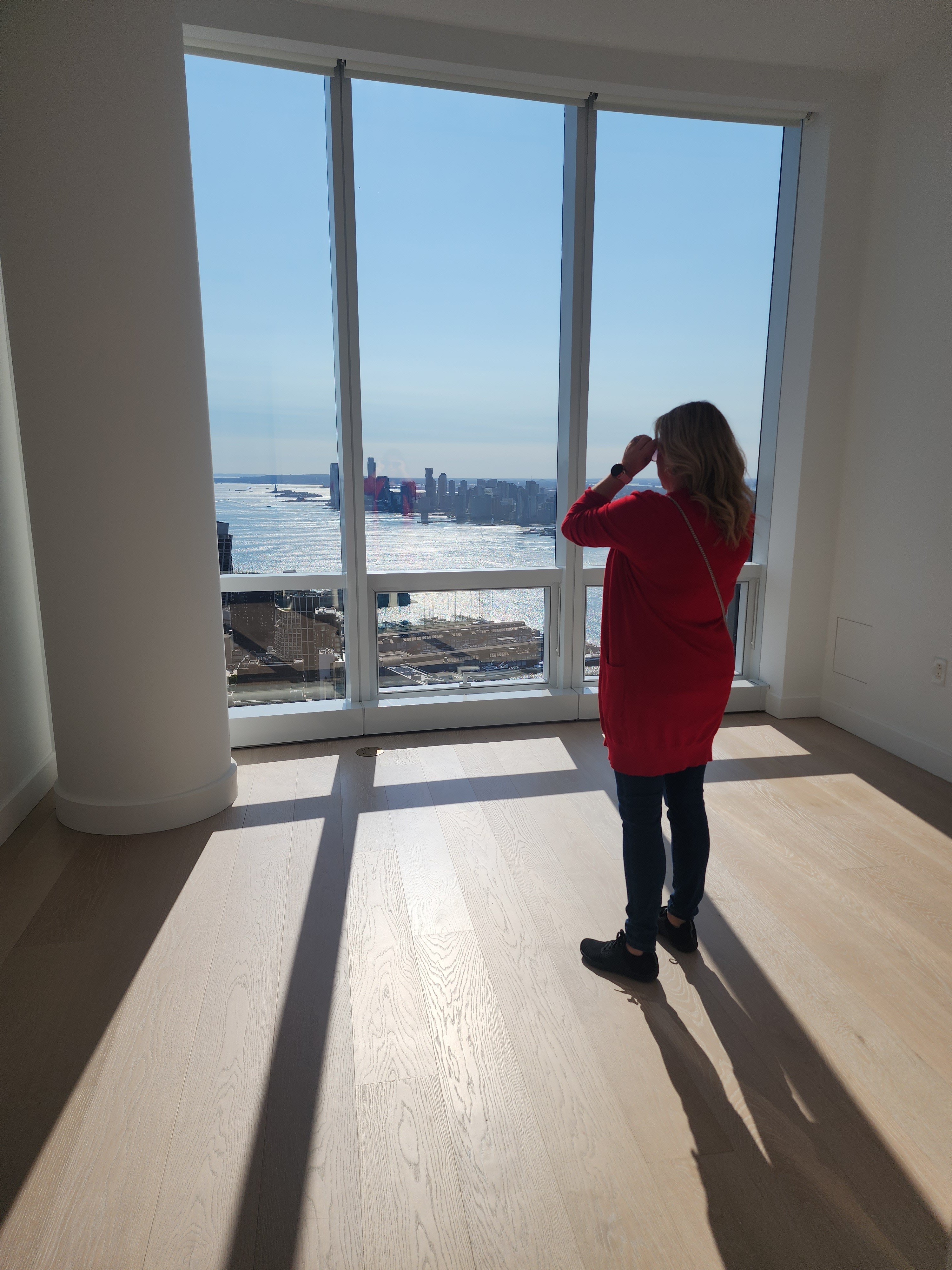 A woman looking out across the Hudson Yards skyline from a sunlit apartment