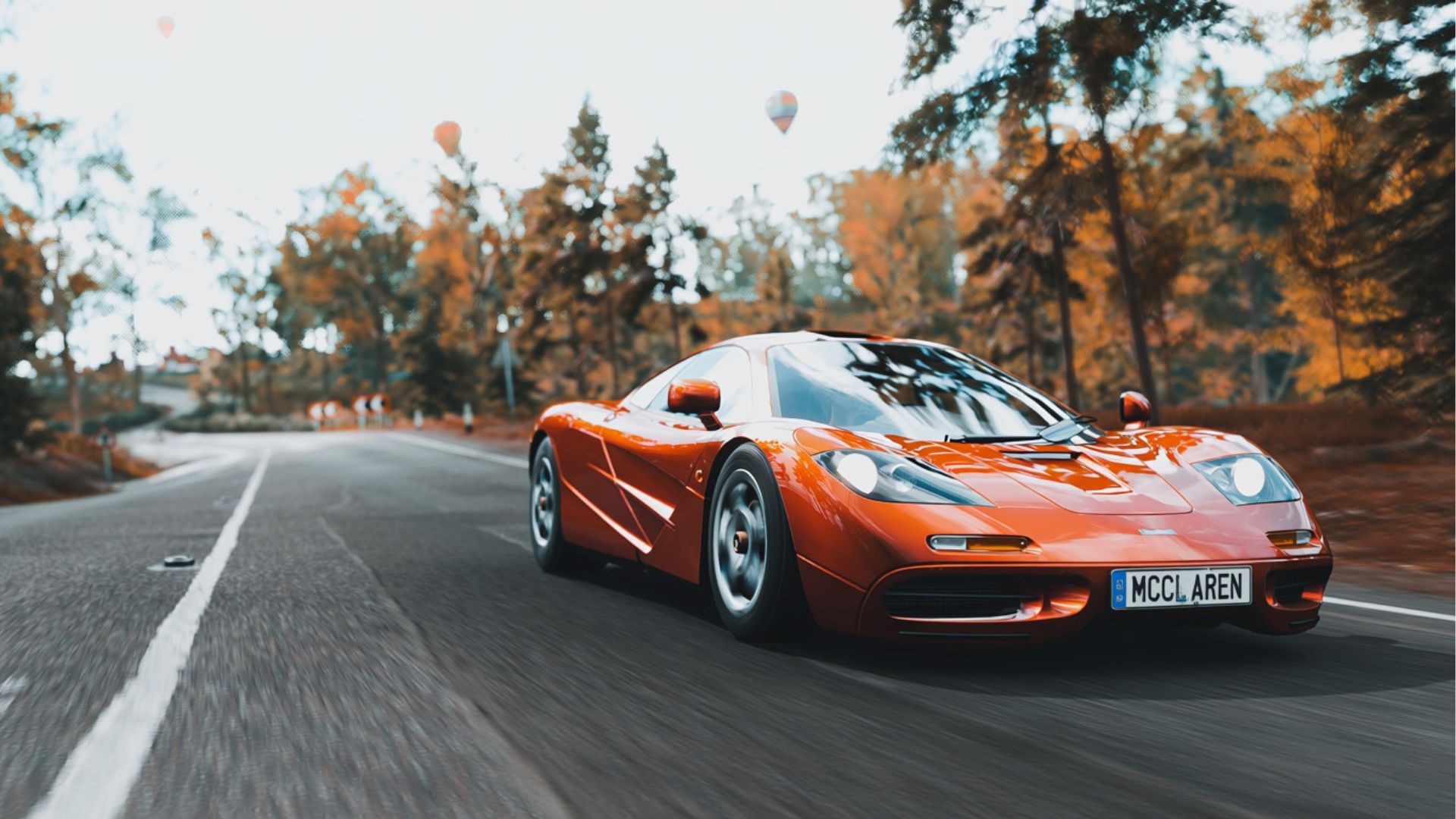 Orange McLaren driving along an autumn tree-lined road