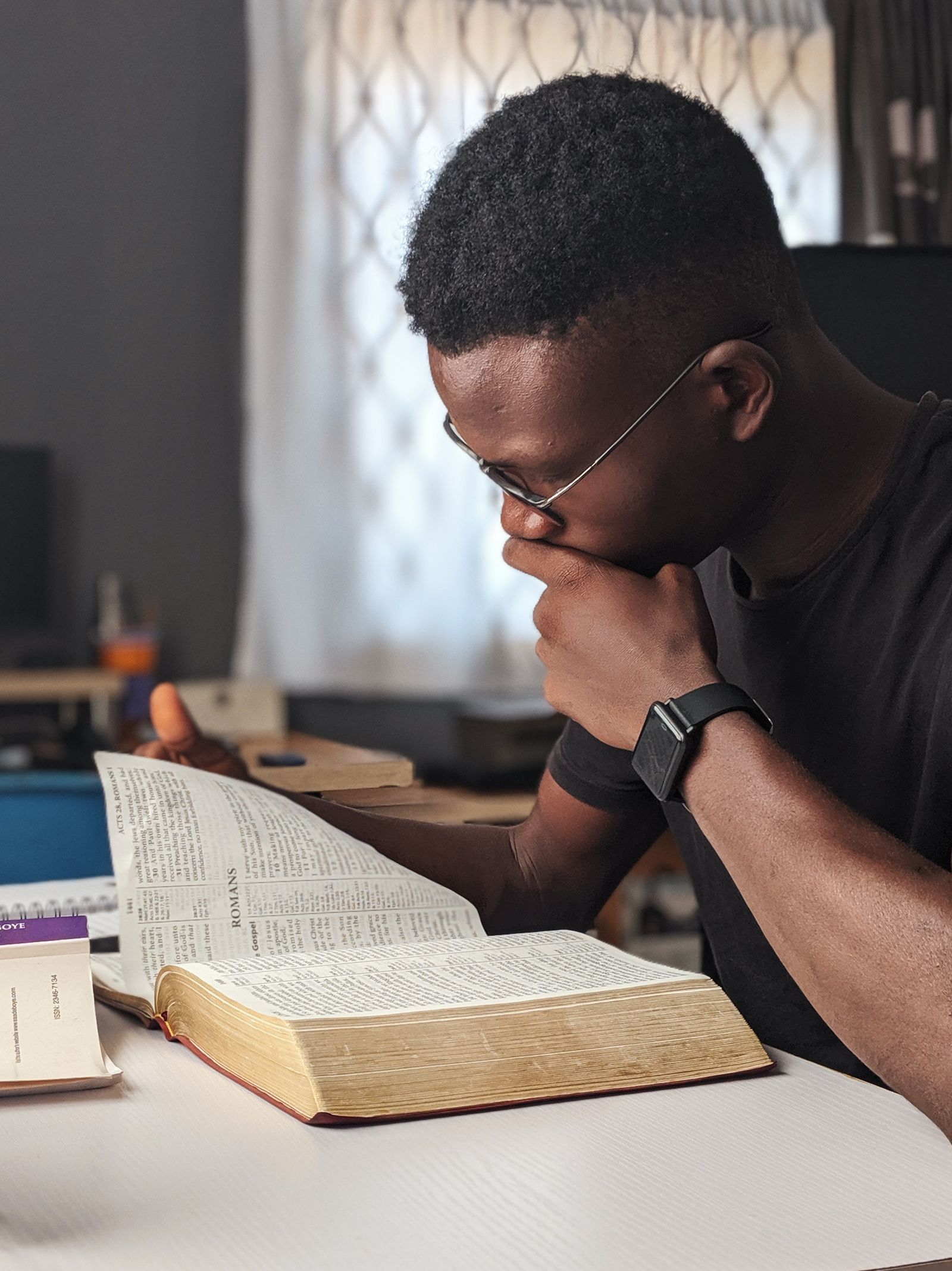 Person thoughtfully reading an open Bible at a desk