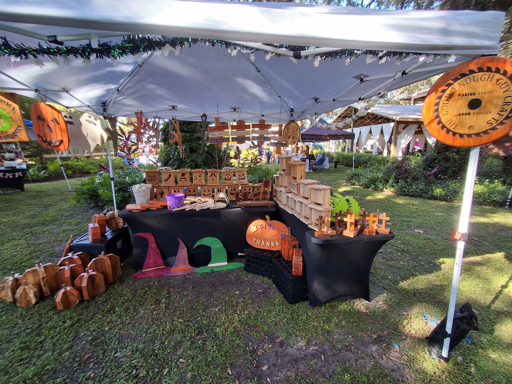 The Good Enough Guy Crafts booth with a wooden shop sign, seasonal lanterns, pumpkins, and crosses