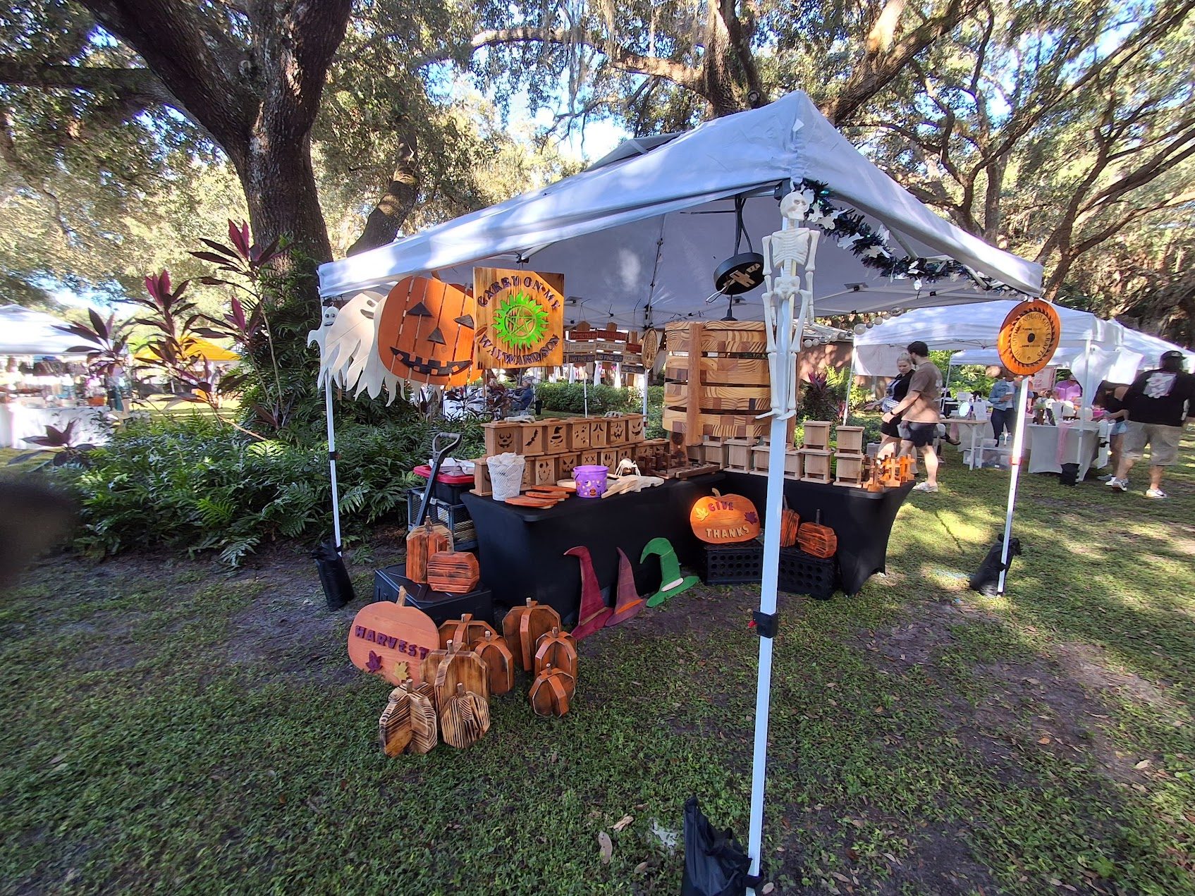 Our outdoor craft-fair booth under the trees with hanging Halloween decorations and wooden crafts